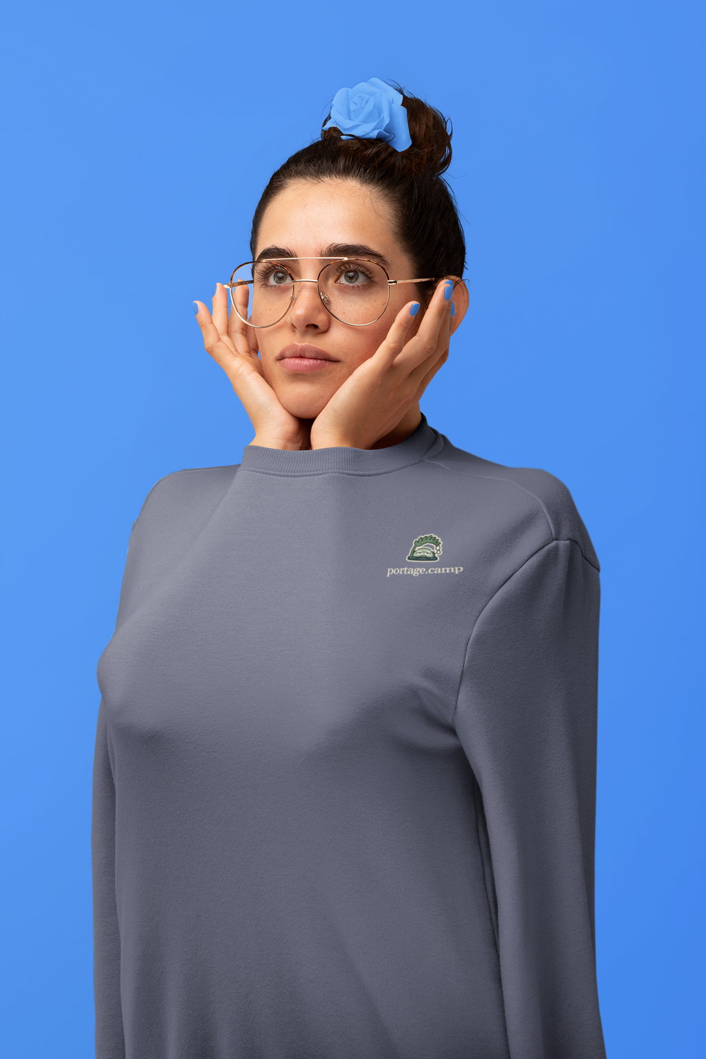 Rain Check Garment-Dyed Crewneck in Denim, worn by a woman in a studio, arms tucked inside the sleeves, with the Rain Check logo and portage.camp on the chest. Digital product mockup.