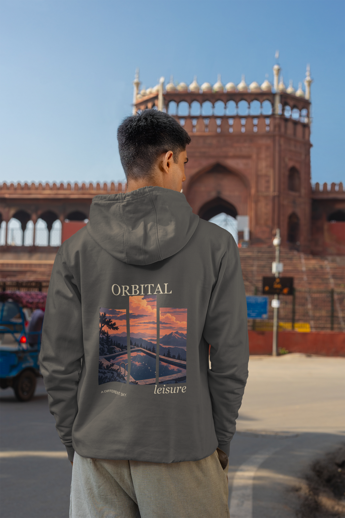 A Different Sky Zip Hoodie in Dark Heather, worn by a man seen from behind on a city street, showing the large print on the back. Digital product mockup.