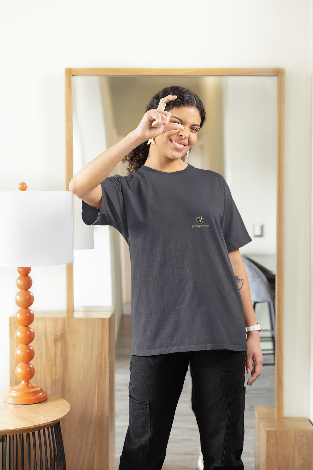 Seen Briefly Garment-Dyed Tee in Navy, worn by a woman at home, pretending to take a photo, with the Seen Briefly logo and portage.camp on the chest. Digital product mockup.