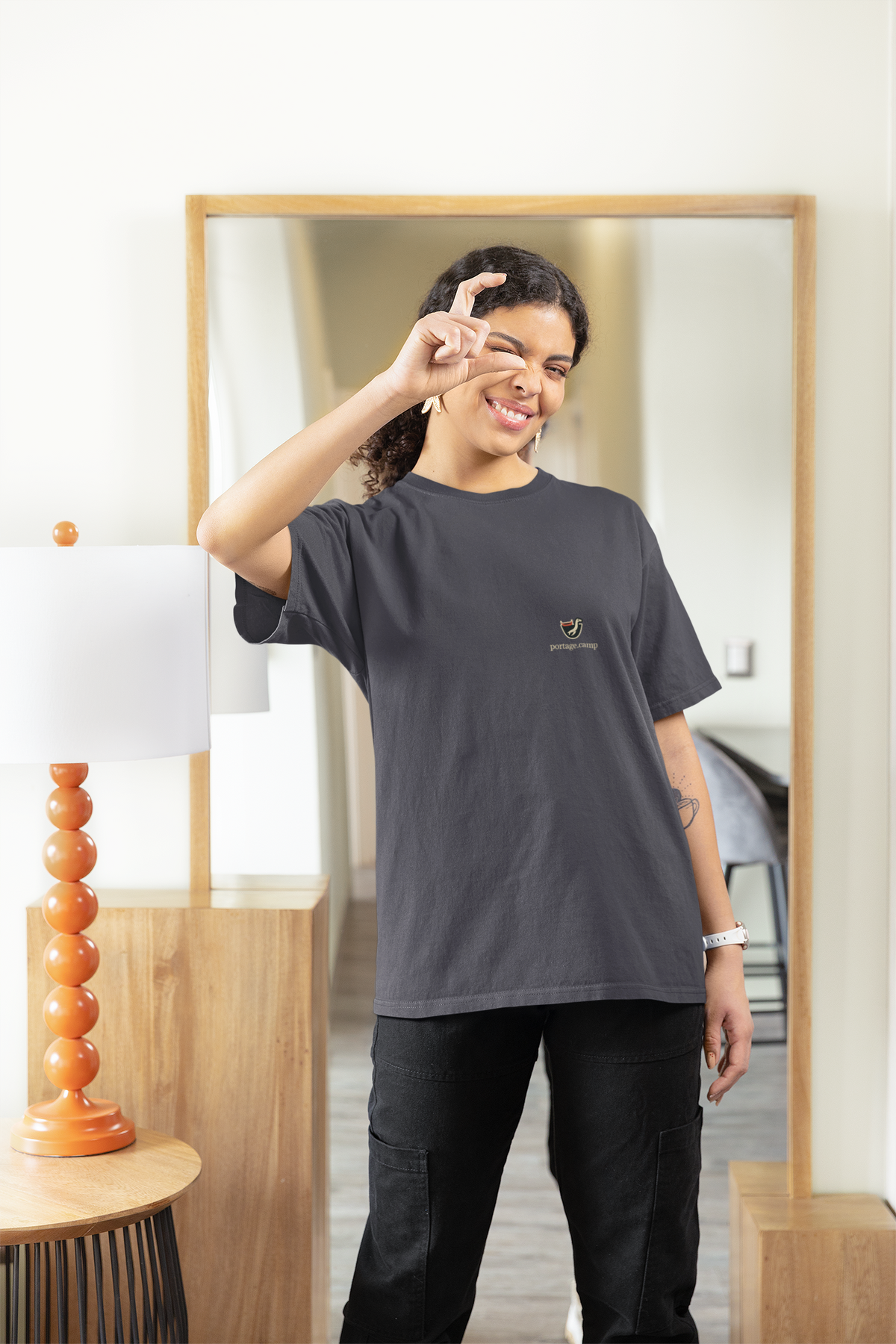 Seen Briefly Garment-Dyed Tee in Navy, worn by a woman at home, pretending to take a photo, with the Seen Briefly logo and portage.camp on the chest. Digital product mockup.