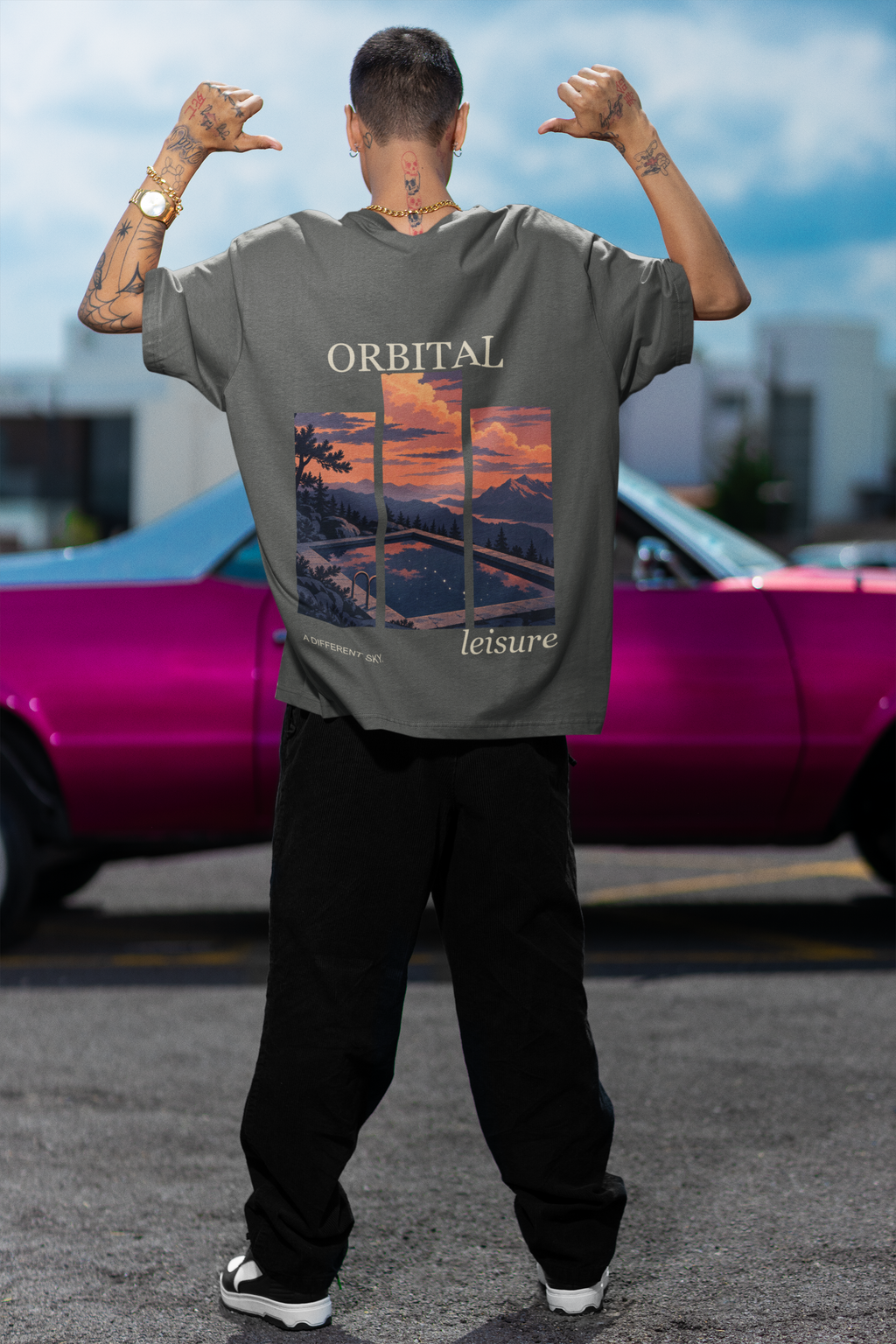 Amethyst After Hours Garment-Dyed Tee in Pepper, worn by a man seen from behind by a pink car, showing the large print on the back. Digital product mockup.