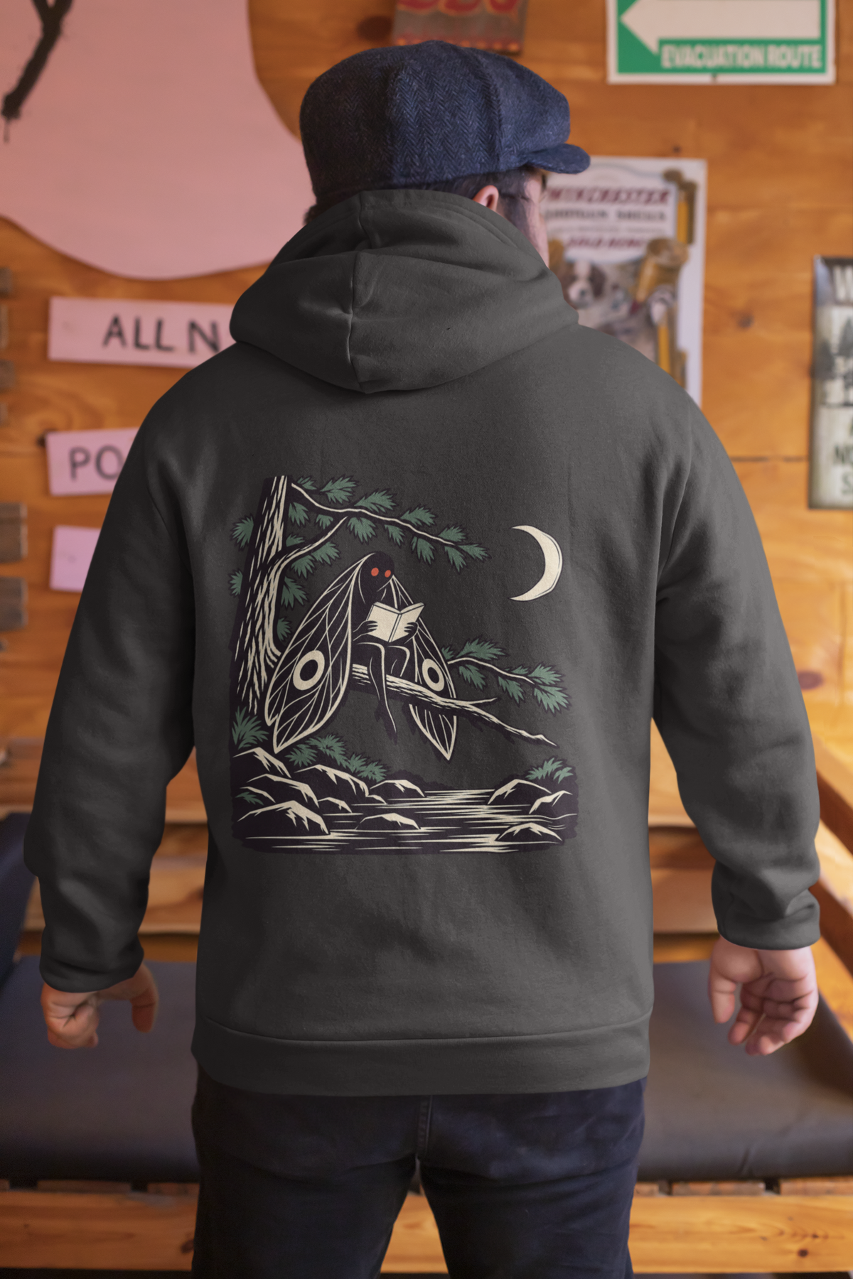 Night Library Zip Hoodie in Black, worn by a man seen from behind in a wood-panelled bar, showing the large print on the back. Digital product mockup.