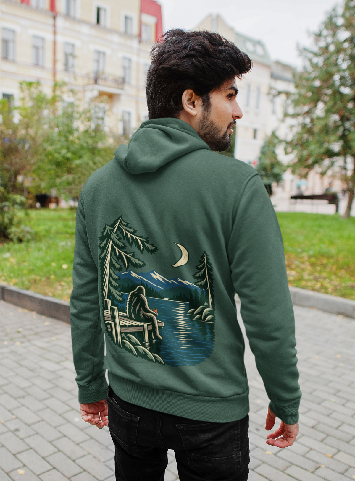 Quiet Hours Midweight Hoodie in Alpine Green, worn by a man seen from behind on a quiet city street, showing the large print on the back. Digital product mockup.