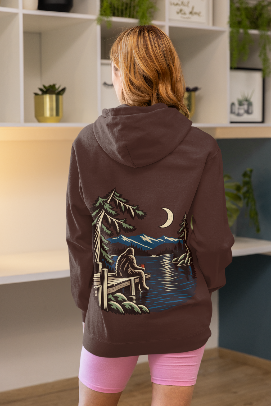 Quiet Hours Heavyweight Hoodie in Brown, worn by a woman seen from behind at home, showing the large print on the back. Digital product mockup.