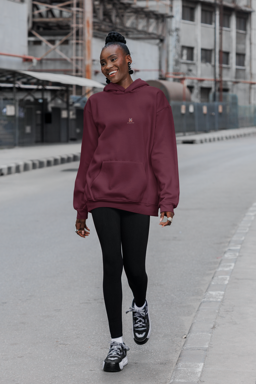 Edge of Evening Midweight Hoodie in Maroon, worn by a woman walking down a city street, with the Edge of Evening logo and portage.camp on the chest. Digital product mockup.