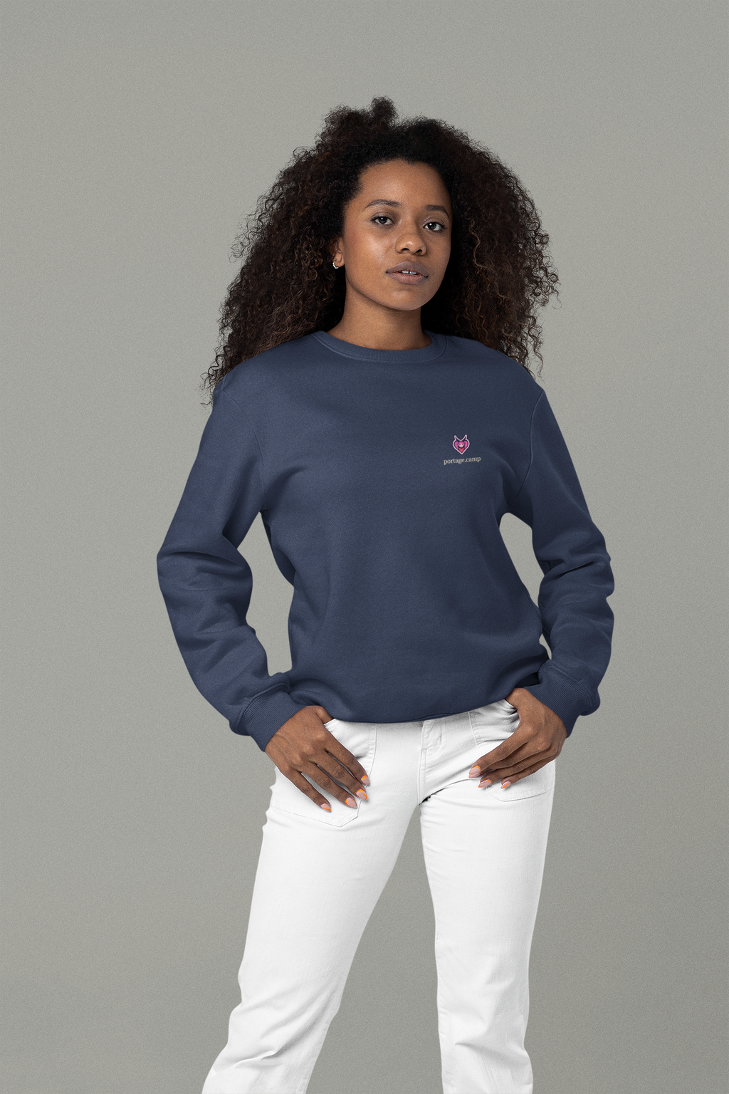 Heart Thief Garment-Dyed Crewneck in True Navy, worn by a woman in a studio with her hands in her pockets, with the Heart Thief logo and portage.camp on the chest. Digital product mockup.