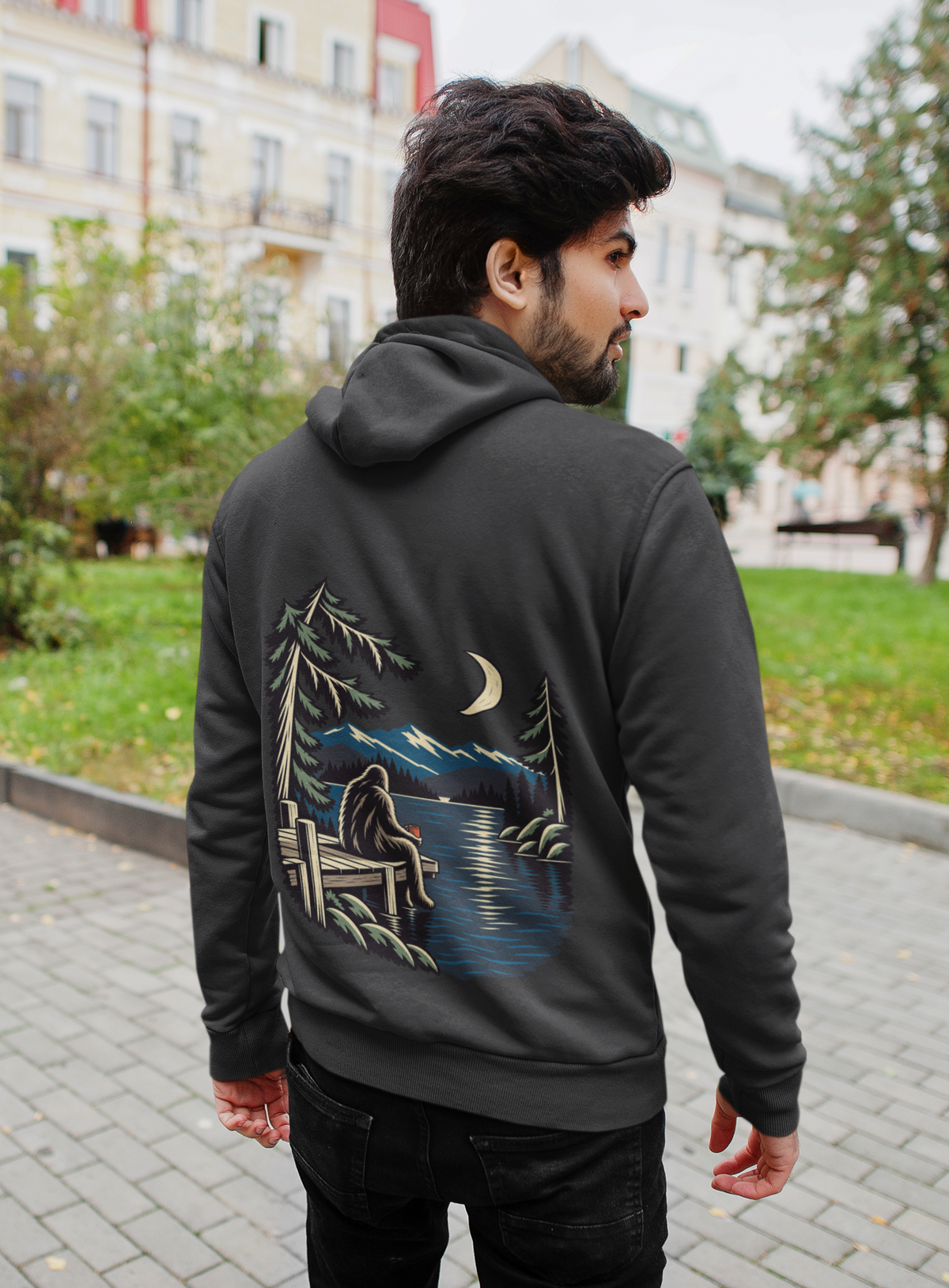 Quiet Hours Heavyweight Hoodie in Black, worn by a man seen from behind on a quiet city street, showing the large print on the back. Digital product mockup.