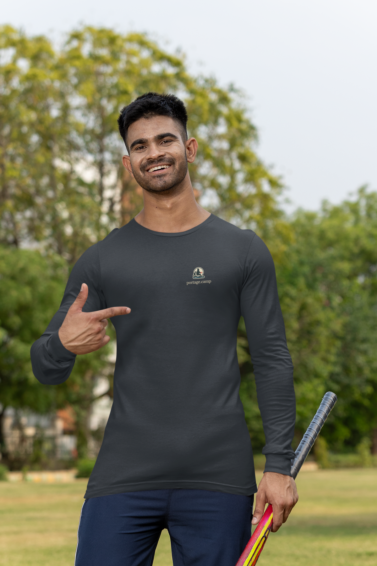 Quiet Hours Garment-Dyed Long-Sleeve Tee in Black, worn by a man at a cricket field, with the Quiet Hours logo and portage.camp on the chest. Digital product mockup.
