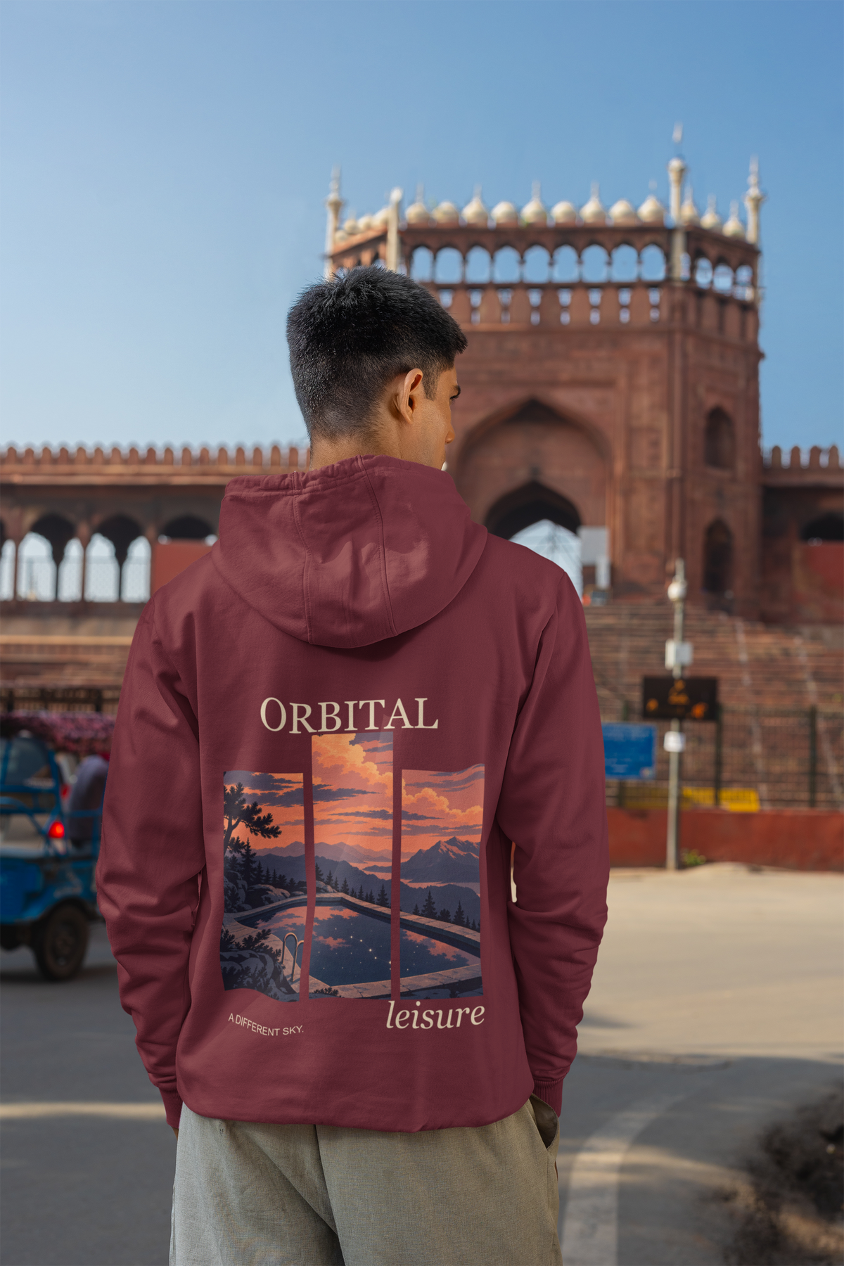 A Different Sky Midweight Hoodie in Maroon, worn by a man seen from behind on a city street, showing the large print on the back. Digital product mockup.