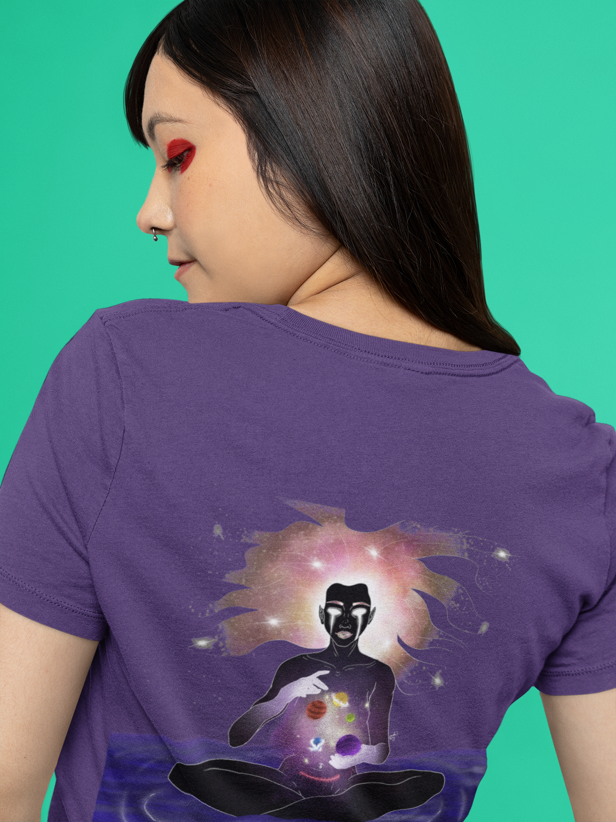 Orbit Keeper Women’s Relaxed Tee in Team Purple, worn by a woman seen from behind against green, showing the large print on the back. Digital product mockup.