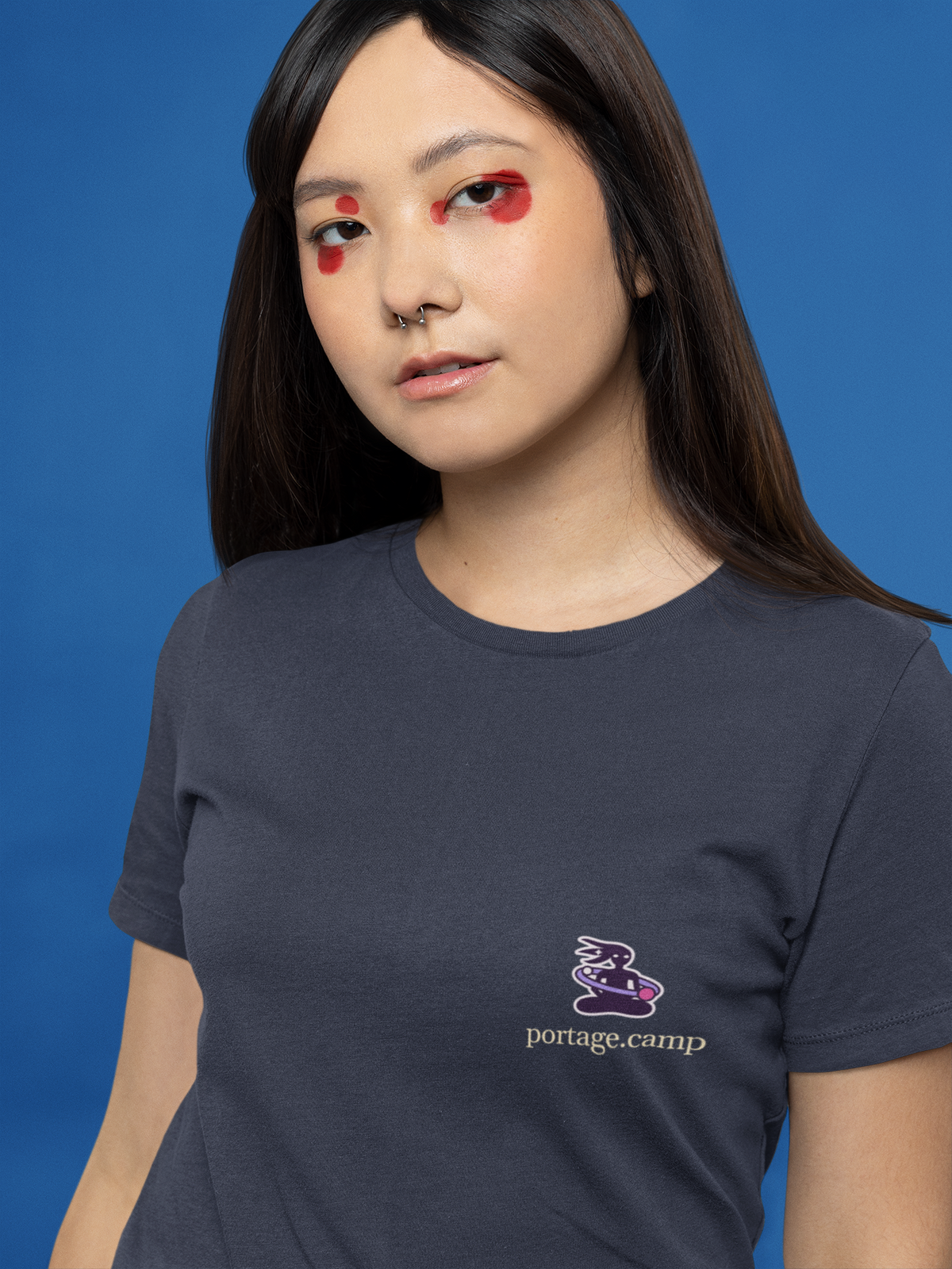 Orbit Keeper Women’s Relaxed Tee in Navy, worn by a woman with graphic eyeliner, close up, with the Orbit Keeper logo and portage.camp on the chest. Digital product mockup.
