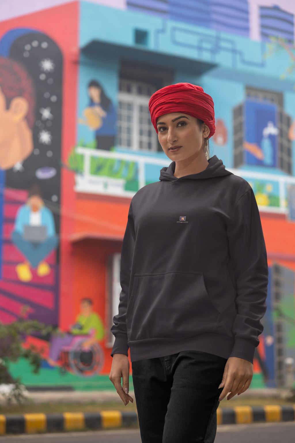Open Late Midweight Hoodie in Black, worn by a woman in a turban on a busy street, with the Open Late logo and portage.camp on the chest. Digital product mockup.