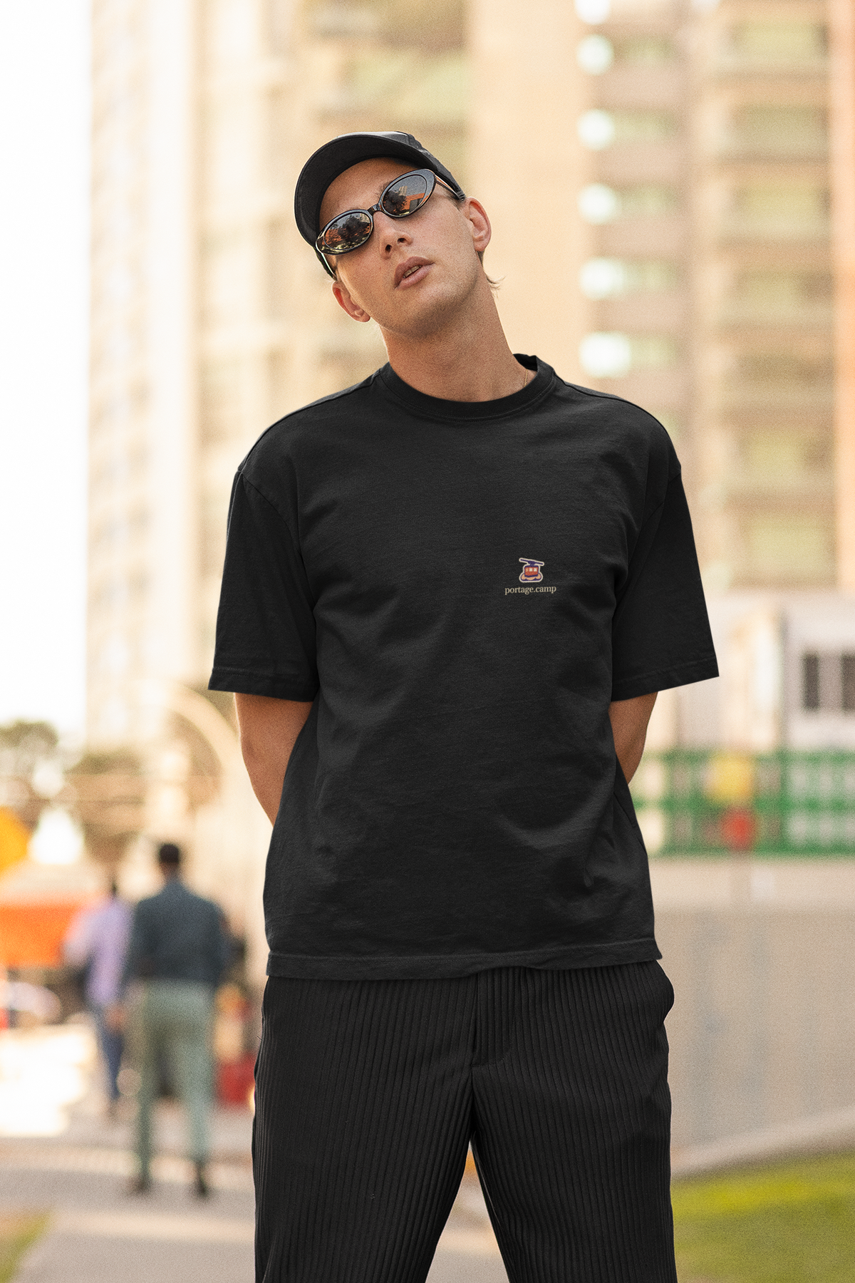 Cloud Ferry Garment-Dyed Tee in Black, worn by a man in a cap and sunglasses on a city street, with the Cloud Ferry logo and portage.camp on the chest. Digital product mockup.