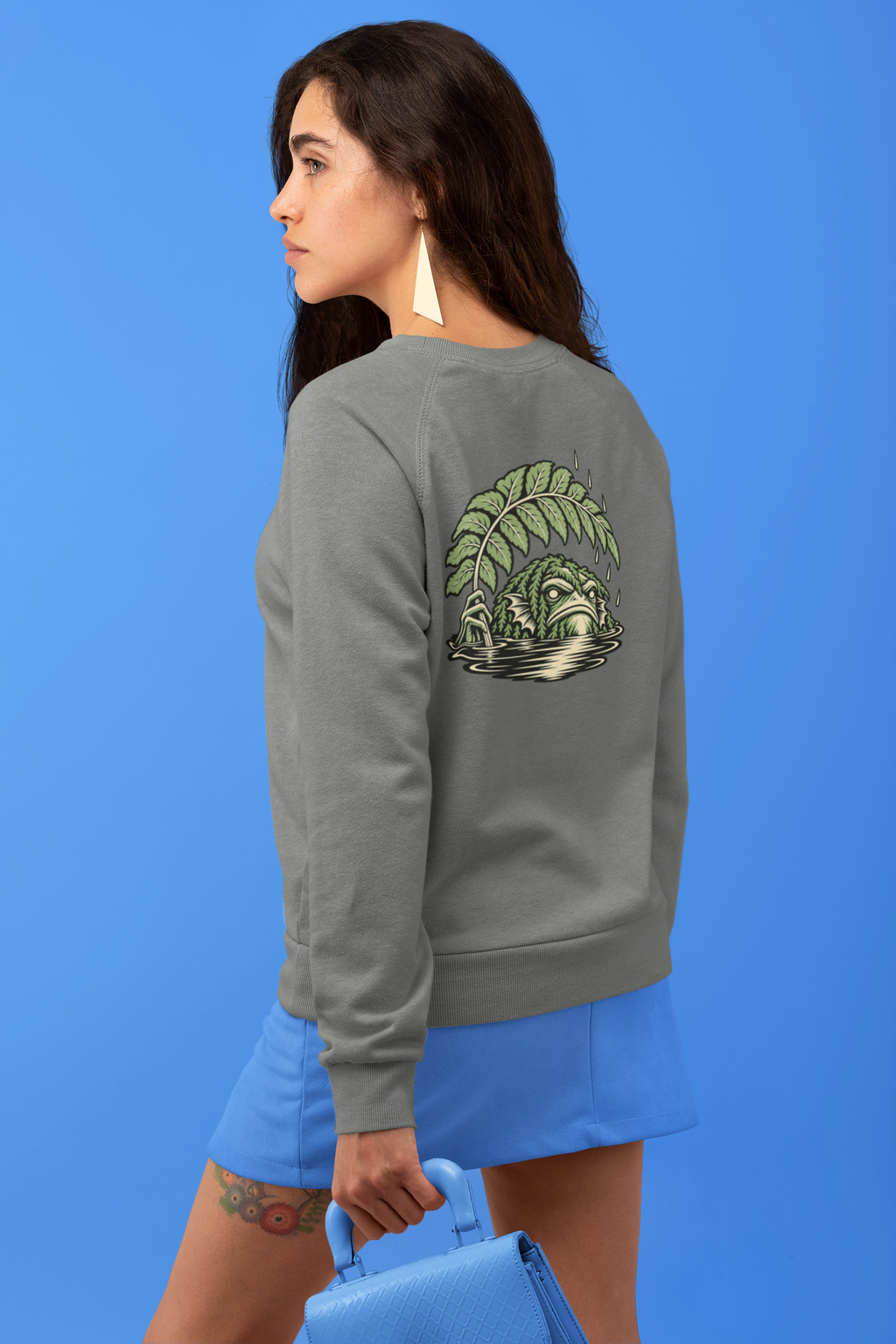 Rain Check Garment-Dyed Crewneck in Pepper, worn by a woman seen from behind against a blue backdrop, showing the large print on the back. Digital product mockup.