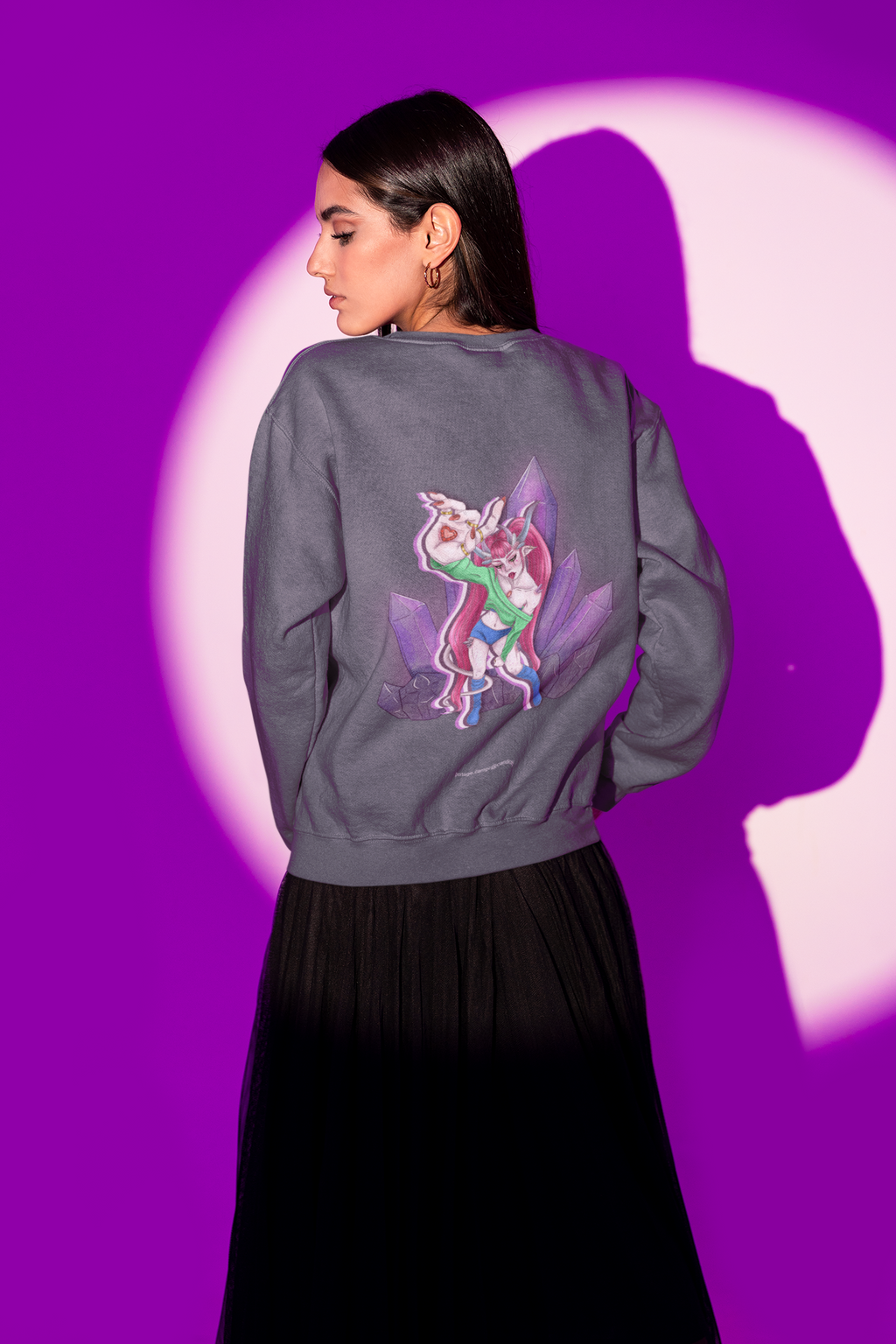 Amethyst After Hours Garment-Dyed Crewneck in Denim, worn by a woman seen from behind in a studio under purple light, showing the large print on the back. Digital product mockup.