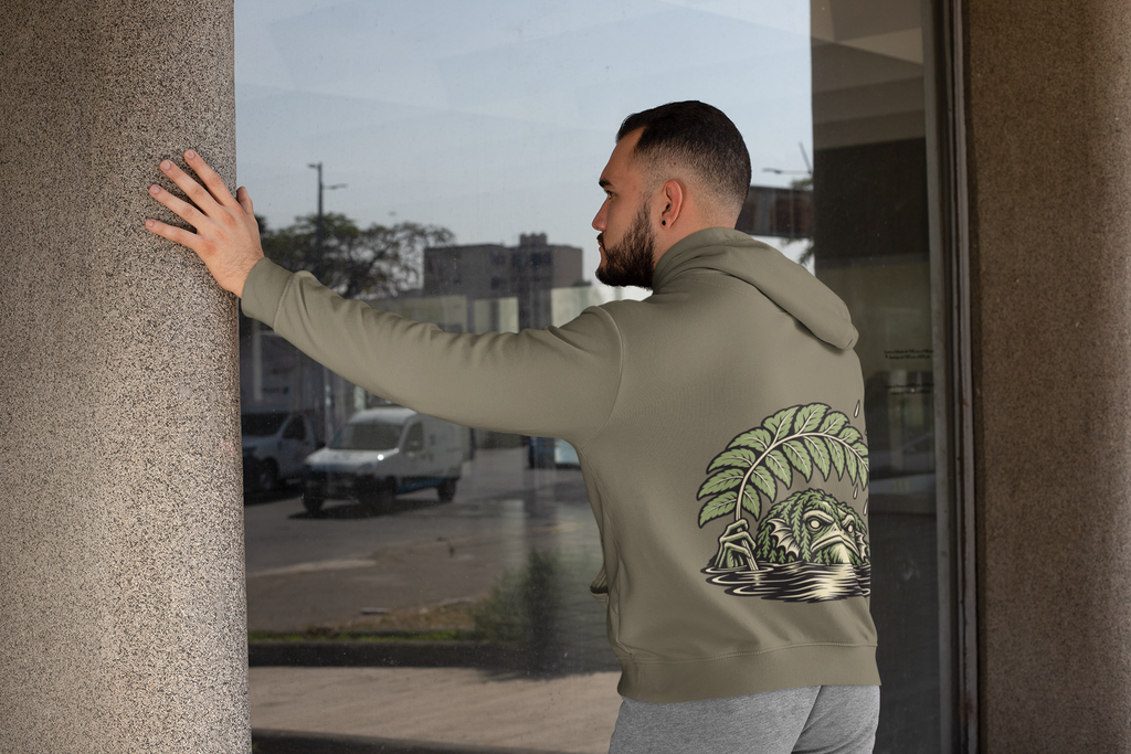 Rain Check Heavyweight Hoodie in Olive, worn by a man seen from behind leaning on a pillar by a window, showing the large print on the back. Digital product mockup.