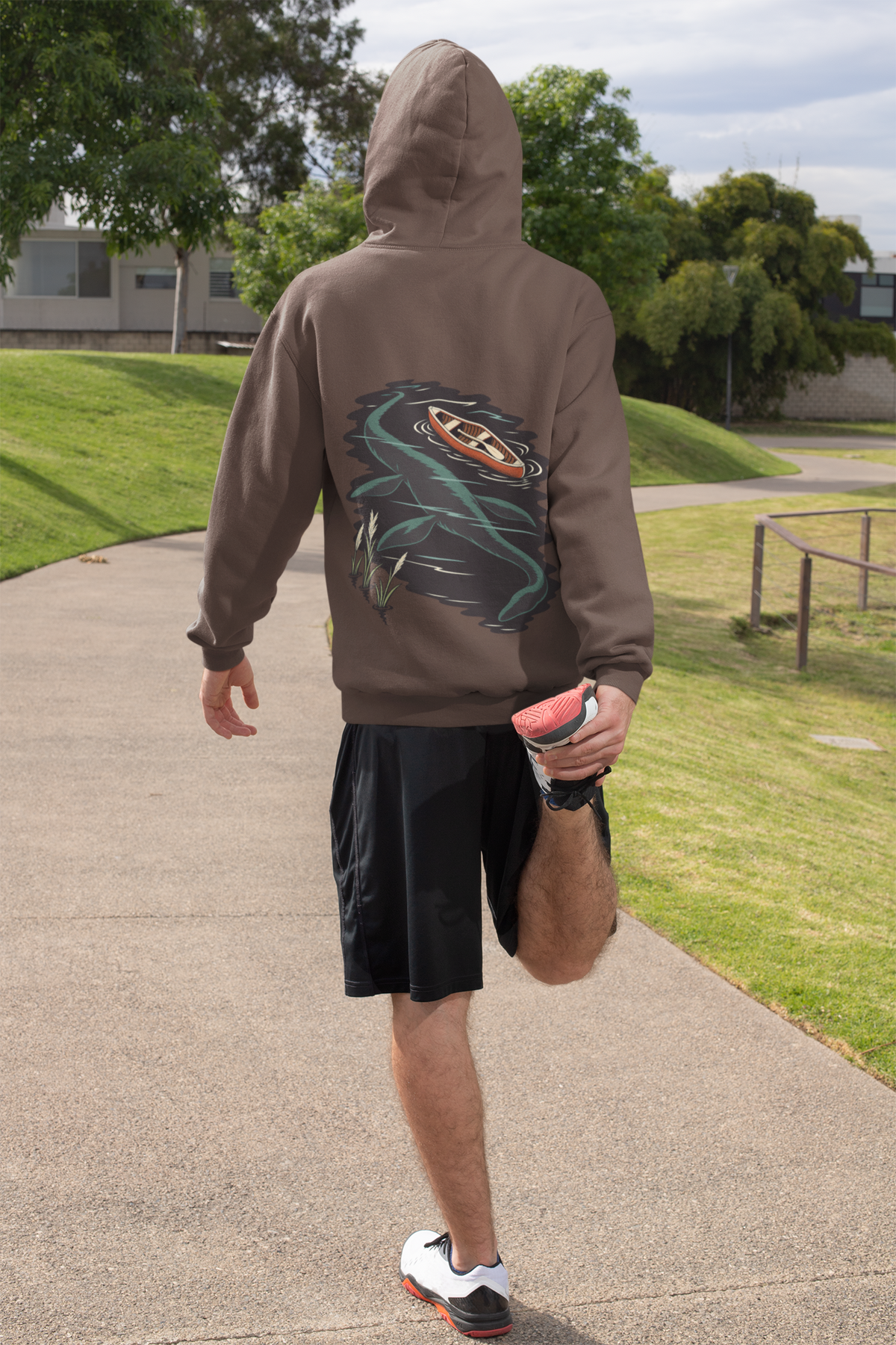 Seen Briefly Heavyweight Hoodie in Brown, worn by a man seen from behind on a sunny path, ready for a run, showing the large print on the back. Digital product mockup.