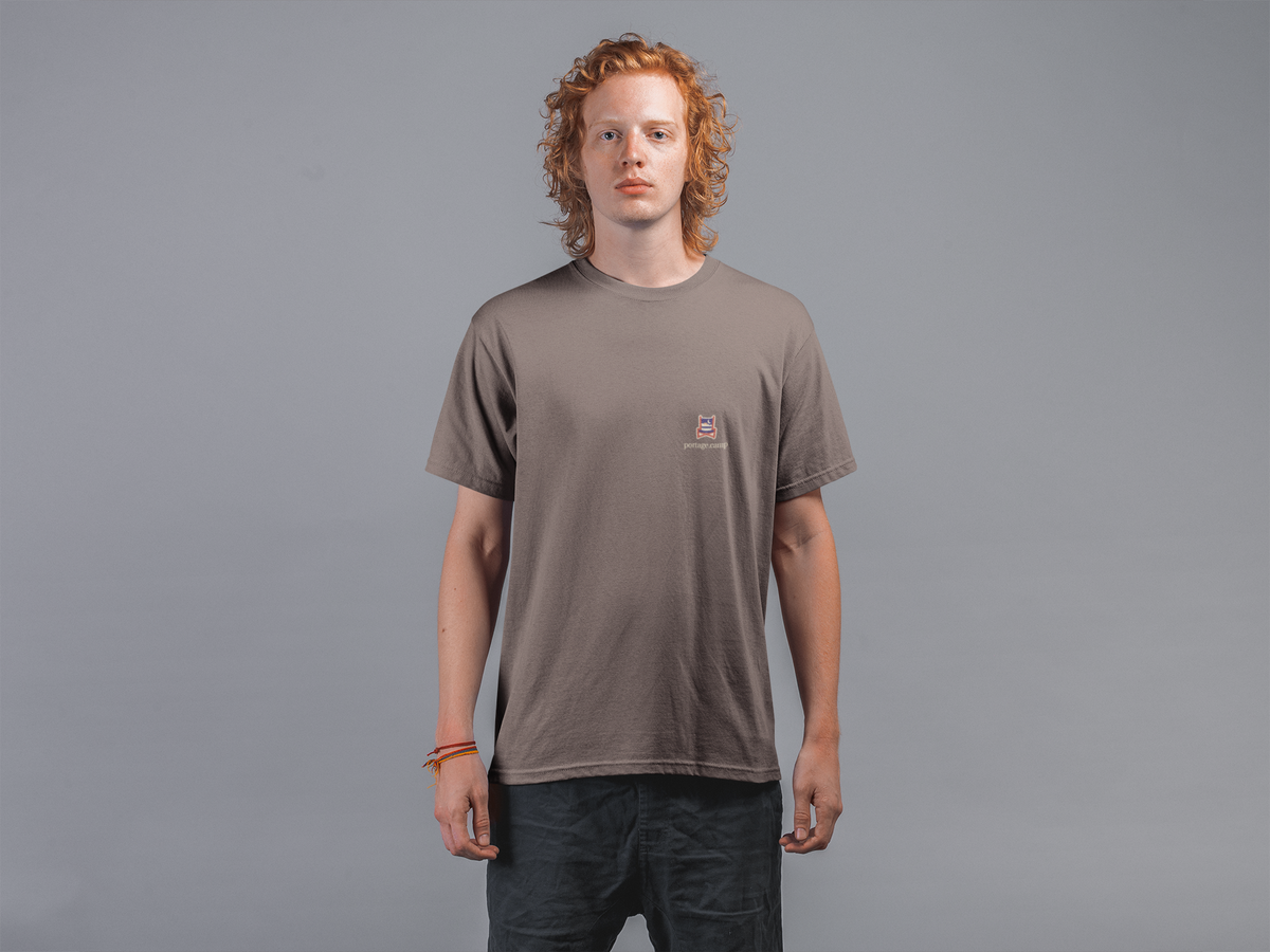 Edge of Evening Garment-Dyed Tee in Espresso, worn by a man against a plain grey wall, with the Edge of Evening logo and portage.camp on the chest. Digital product mockup.