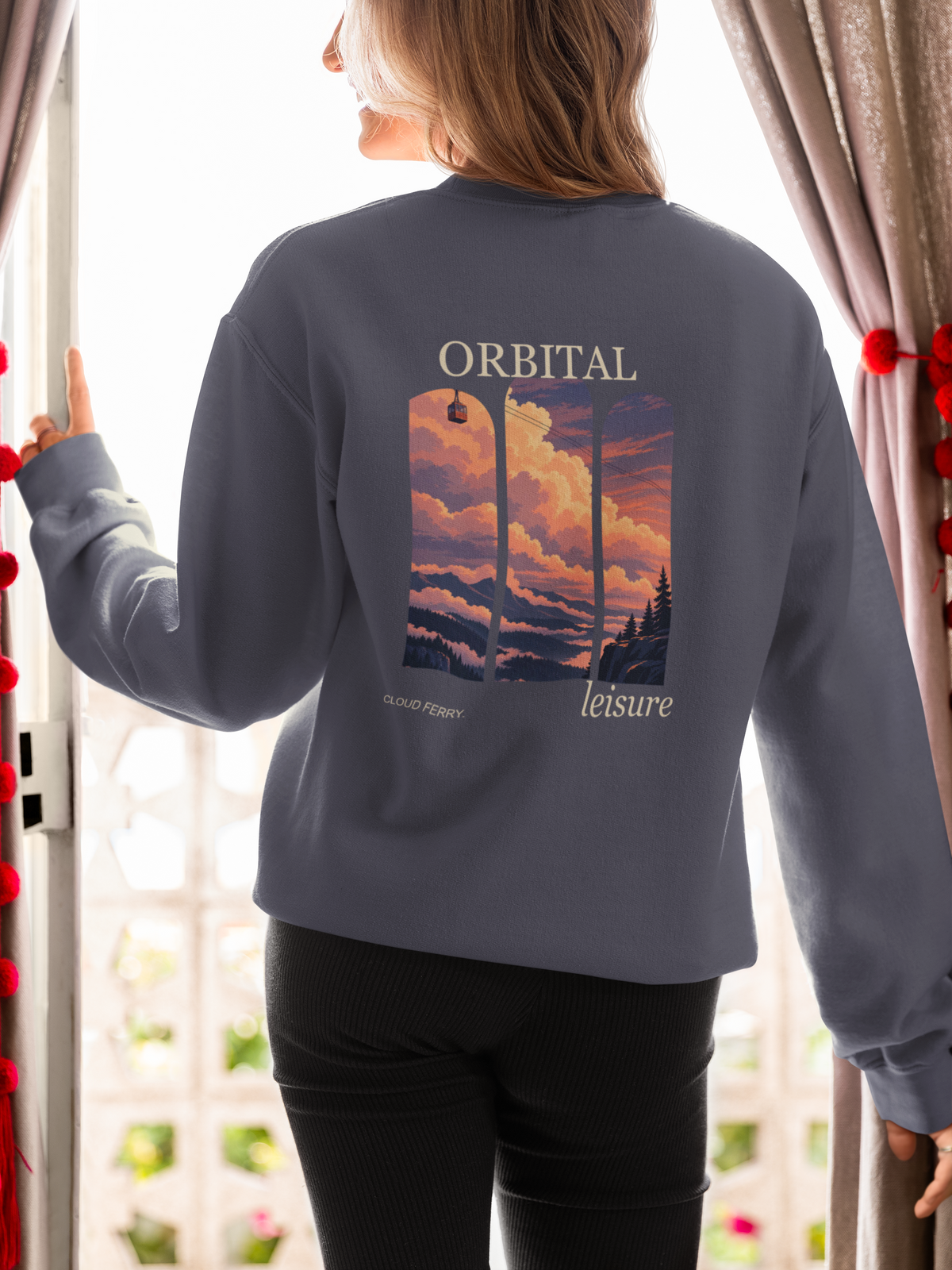 Cloud Ferry Garment-Dyed Crewneck in Denim, worn by a woman seen from behind at an open door, showing the large print on the back. Digital product mockup.