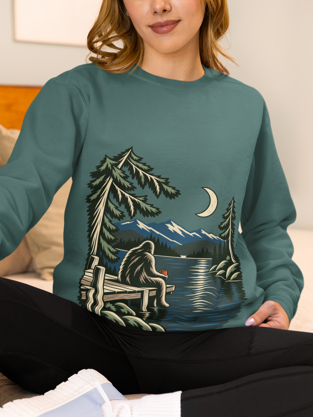 Quiet Hours Garment-Dyed Crewneck (Front Print) in Blue Spruce, worn by a woman at home, showing the large print on the front. Digital product mockup.
