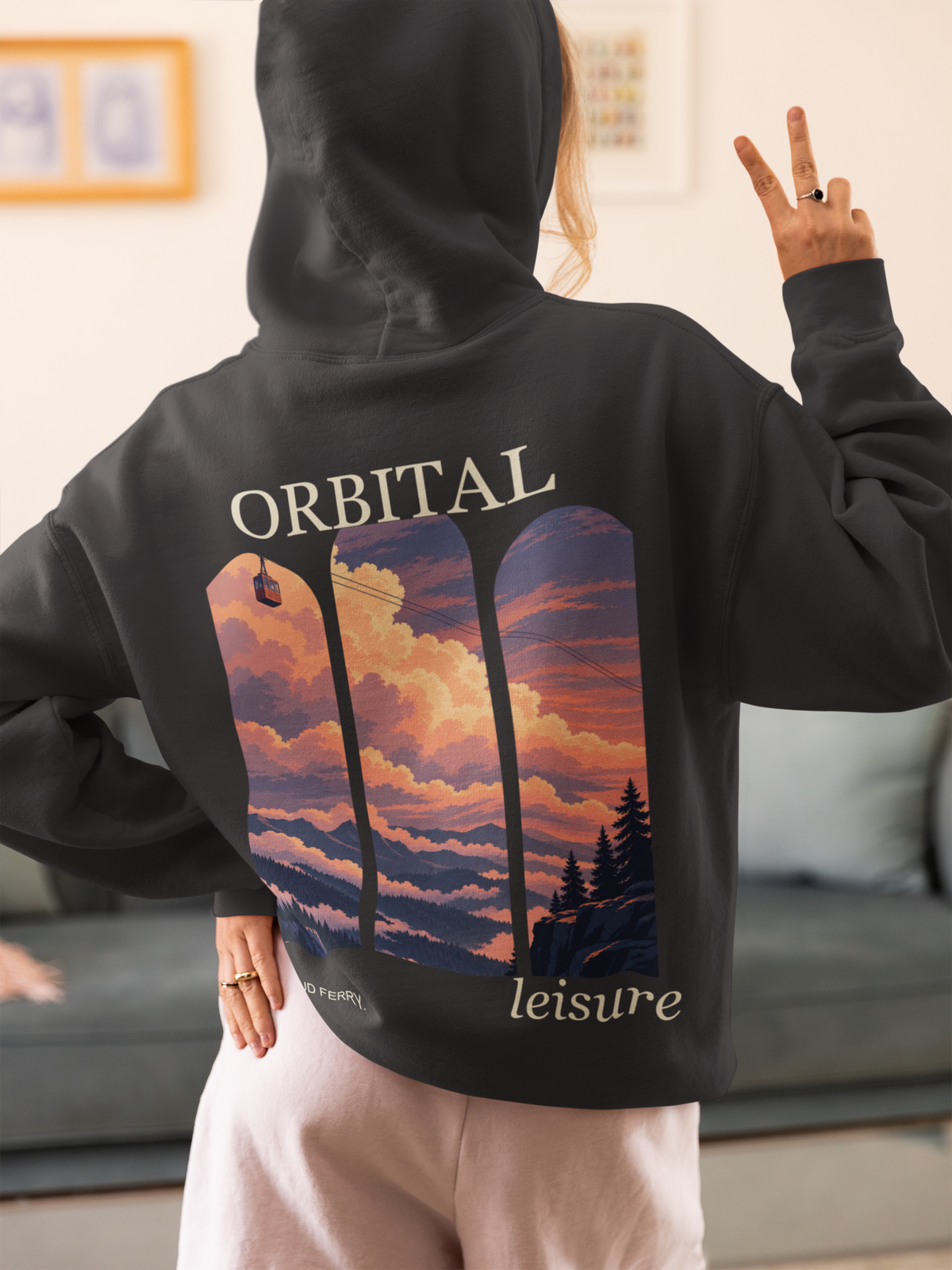 Cloud Ferry Heavyweight Hoodie in Black, worn by a woman seen from behind at home, making a peace sign, showing the large print on the back. Digital product mockup.