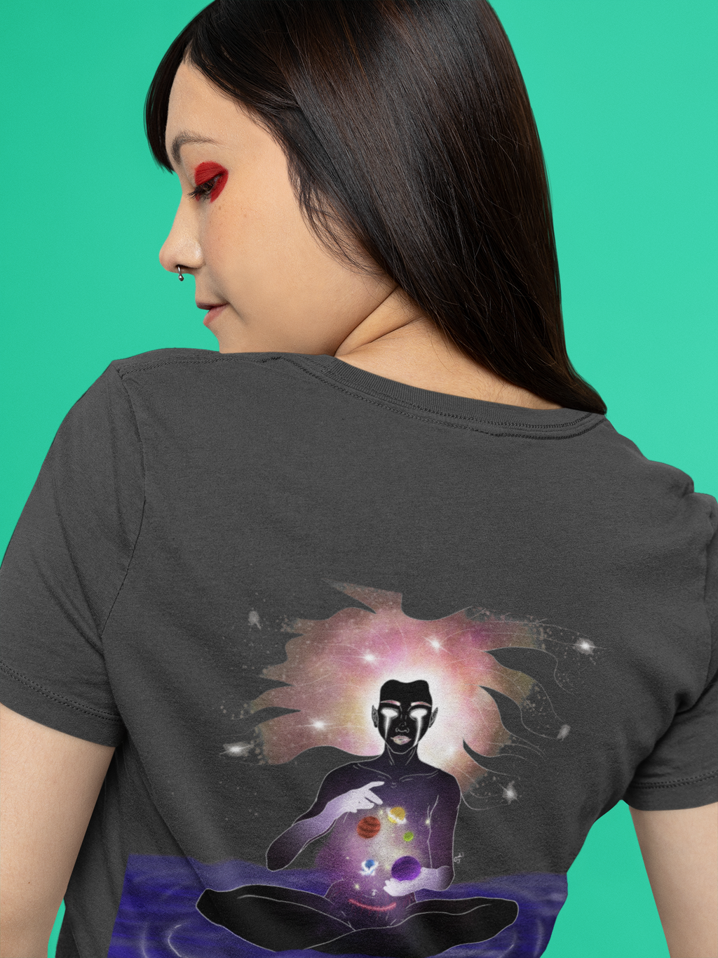 Orbit Keeper Women’s Relaxed Tee in Black, worn by a woman seen from behind against green, showing the large print on the back. Digital product mockup.