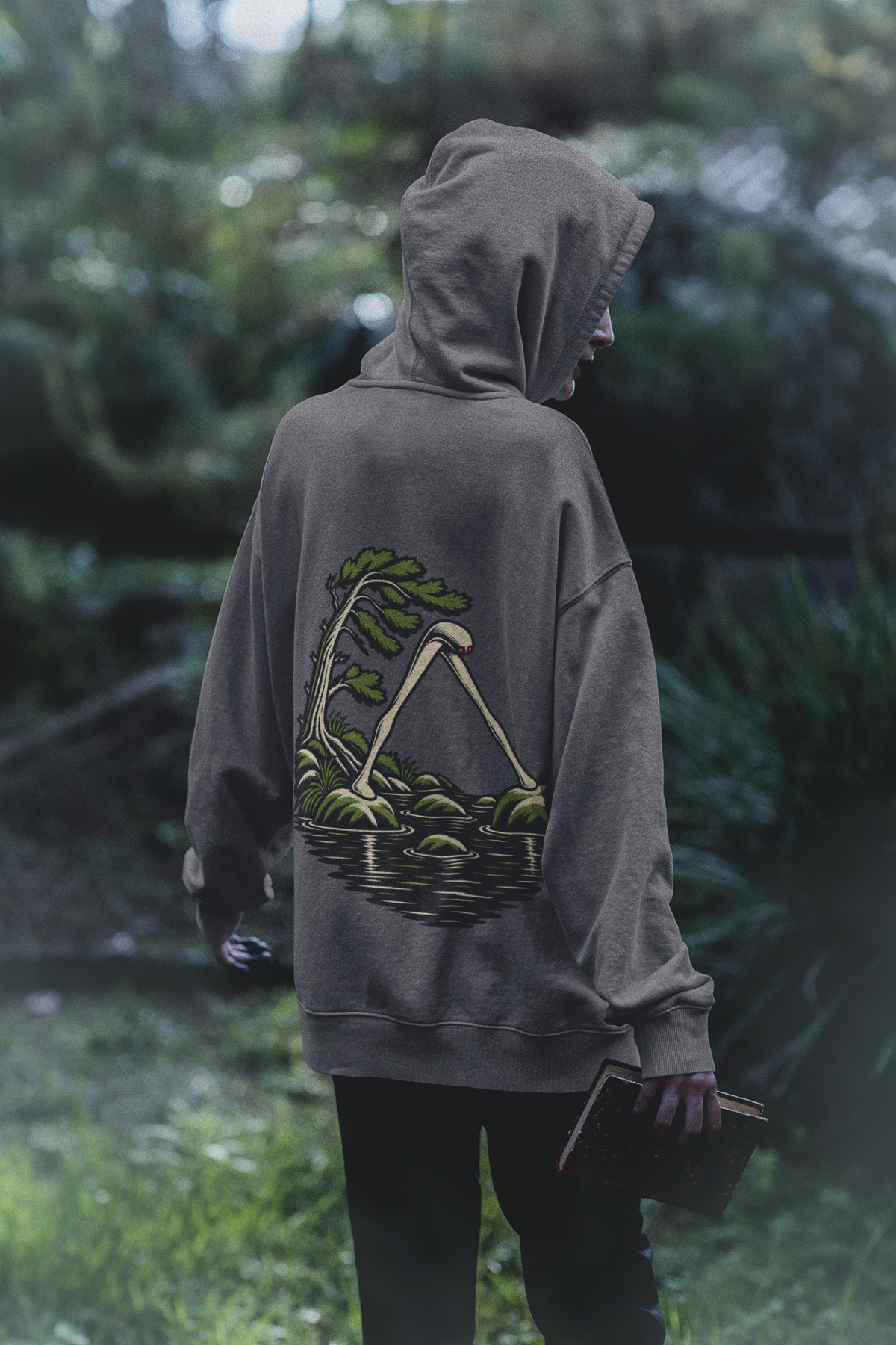 Small Hours Midweight Hoodie in Charcoal, worn by a woman seen from behind in a dark forest, showing the large print on the back. Digital product mockup.