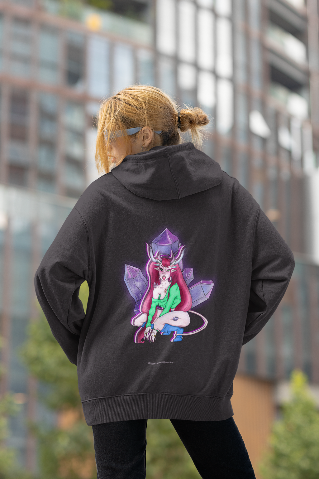 Heart Thief Midweight Hoodie in Black, worn by a woman seen from behind by tall city buildings, showing the large print on the back. Digital product mockup.