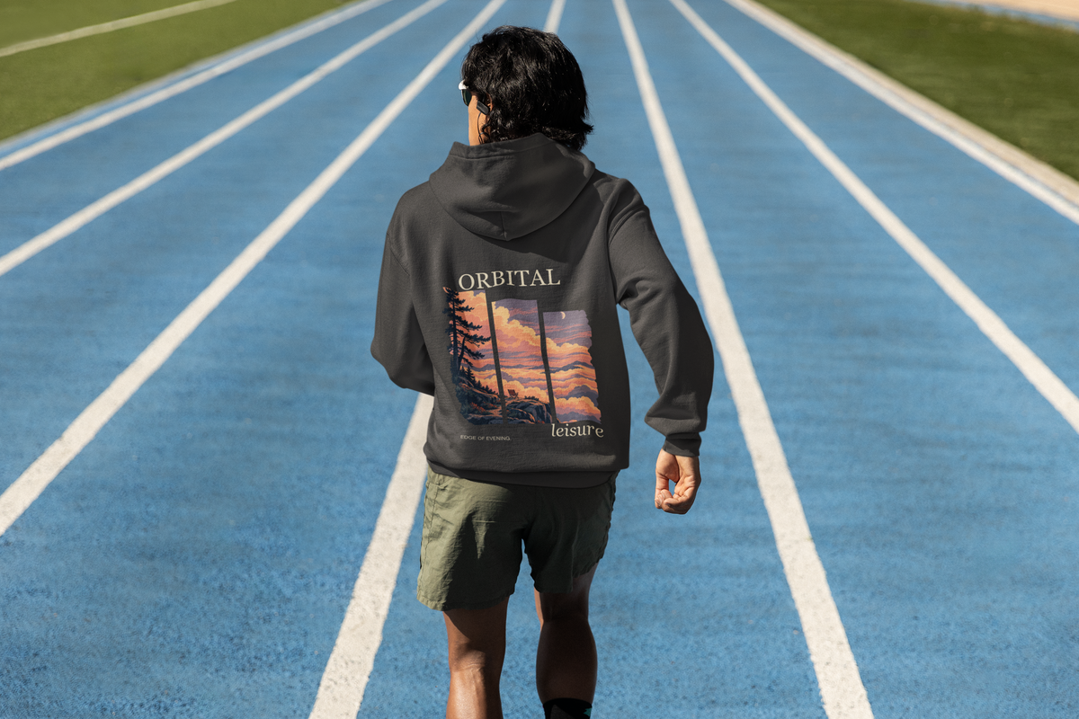 Edge of Evening Heavyweight Hoodie in Black, worn by a man seen from behind on a running track, showing the large print on the back. Digital product mockup.