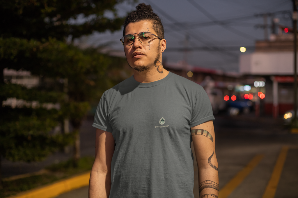 Rain Check Garment-Dyed Tee in Pepper, worn by a man on a street at dusk, with the Rain Check logo and portage.camp on the chest. Digital product mockup.