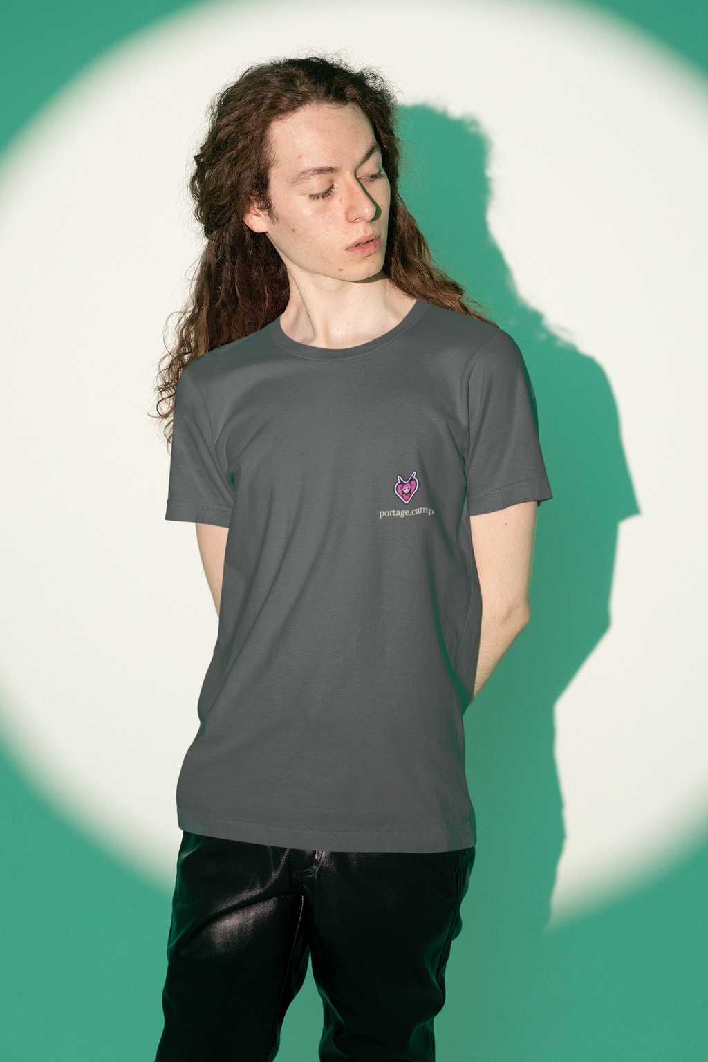 Heart Thief Garment-Dyed Tee in Graphite, worn by a man against green studio light, with the Heart Thief logo and portage.camp on the chest. Digital product mockup.