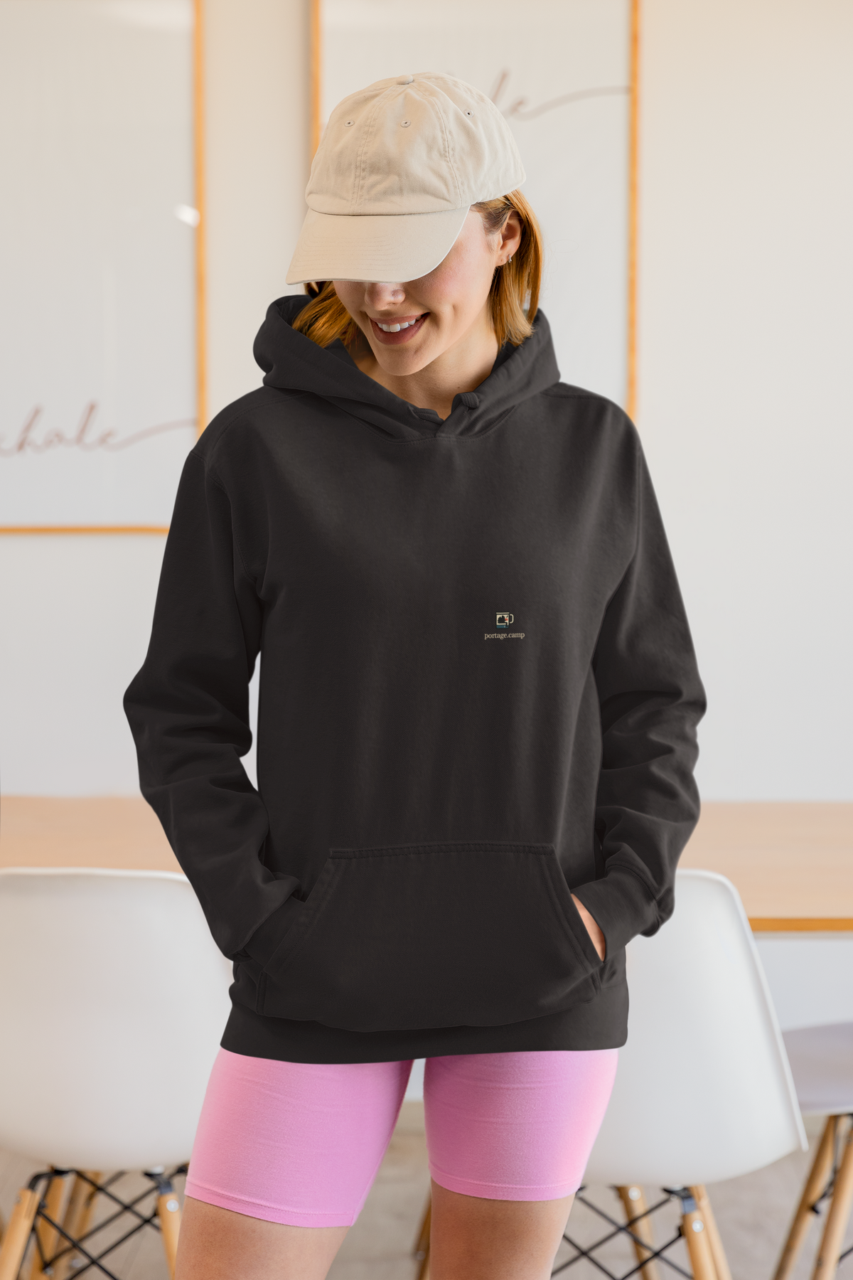 Quiet Hours Heavyweight Hoodie in Black, worn by a woman at home, with the Quiet Hours logo and portage.camp on the left chest. Digital product mockup.