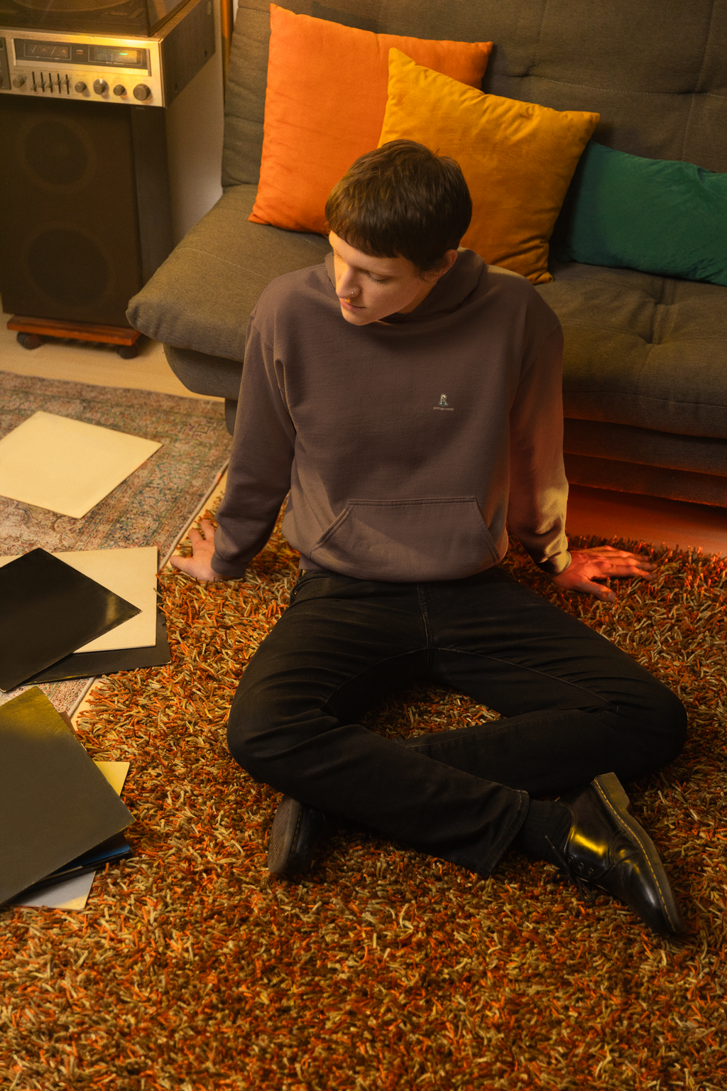 Small Hours Heavyweight Hoodie in Brown, worn by a man seated on the floor among records, with the Small Hours logo and portage.camp on the left chest. Digital product mockup.