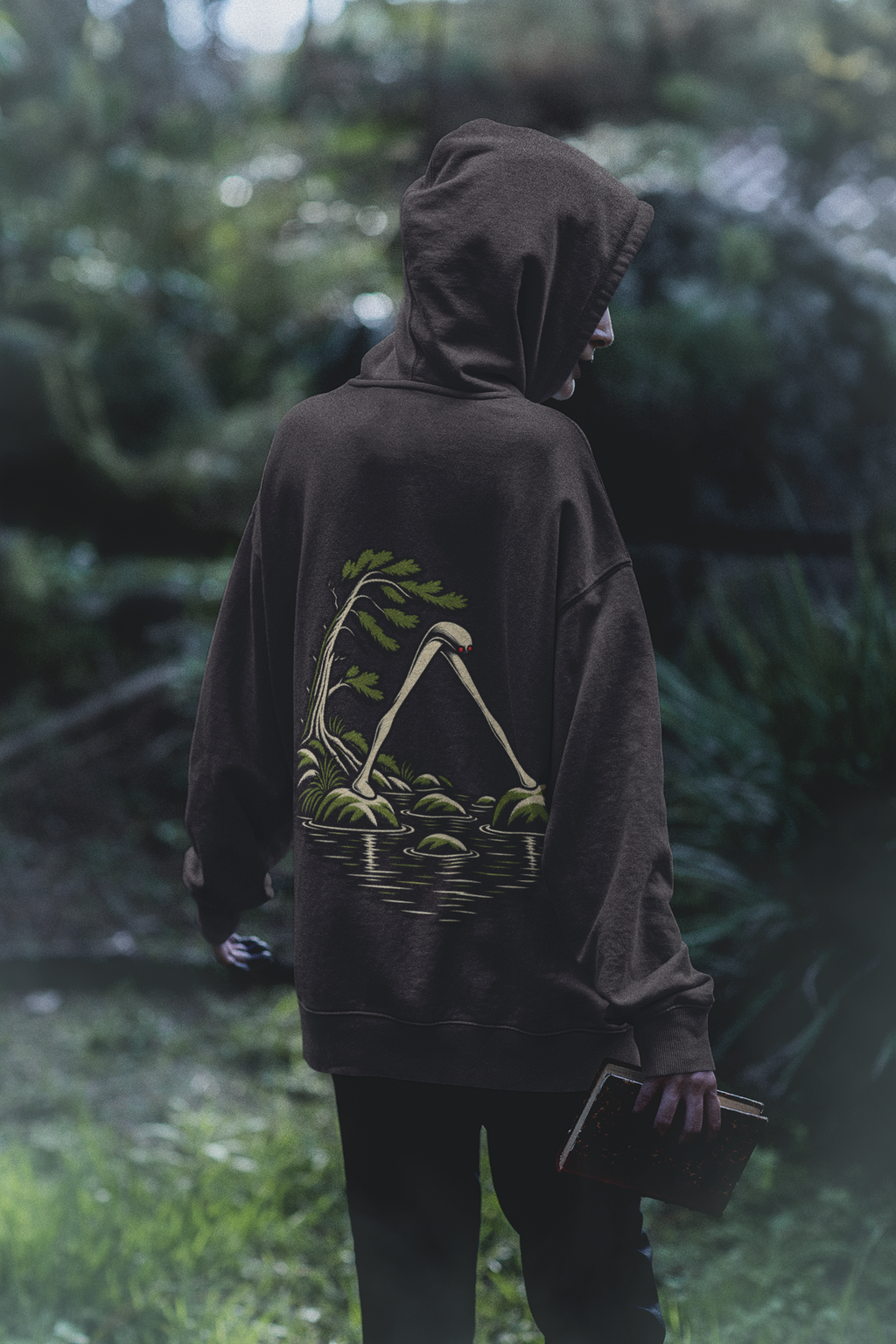 Small Hours Midweight Hoodie in Black, worn by a woman seen from behind in a dark forest, showing the large print on the back. Digital product mockup.