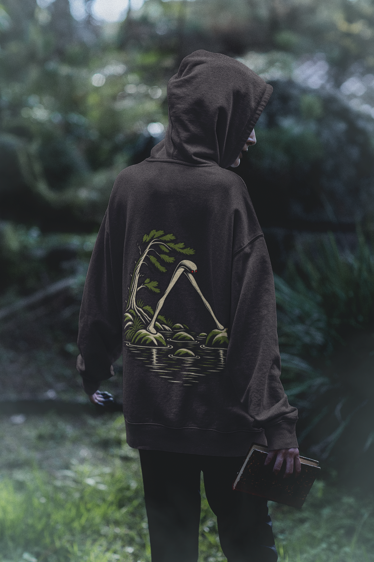 Small Hours Midweight Hoodie in Black, worn by a woman seen from behind in a dark forest, showing the large print on the back. Digital product mockup.
