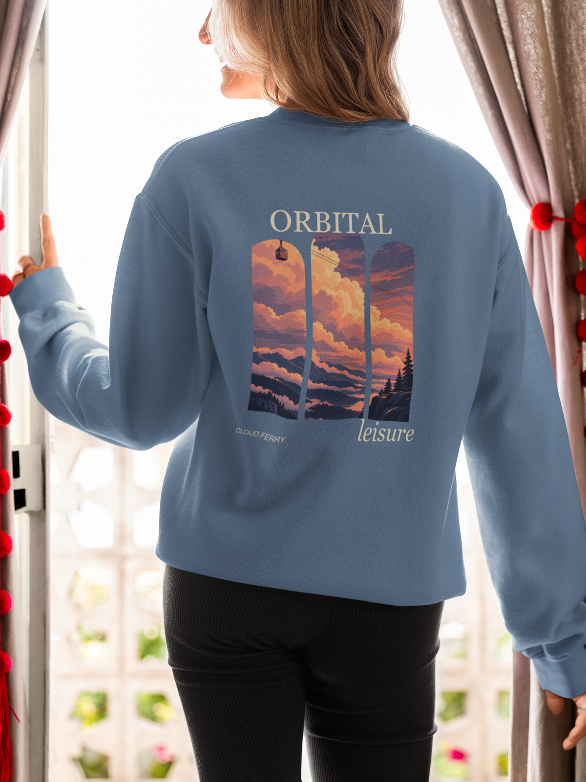 Cloud Ferry Garment-Dyed Crewneck in Blue Jean, worn by a woman seen from behind at an open door, showing the large print on the back. Digital product mockup.