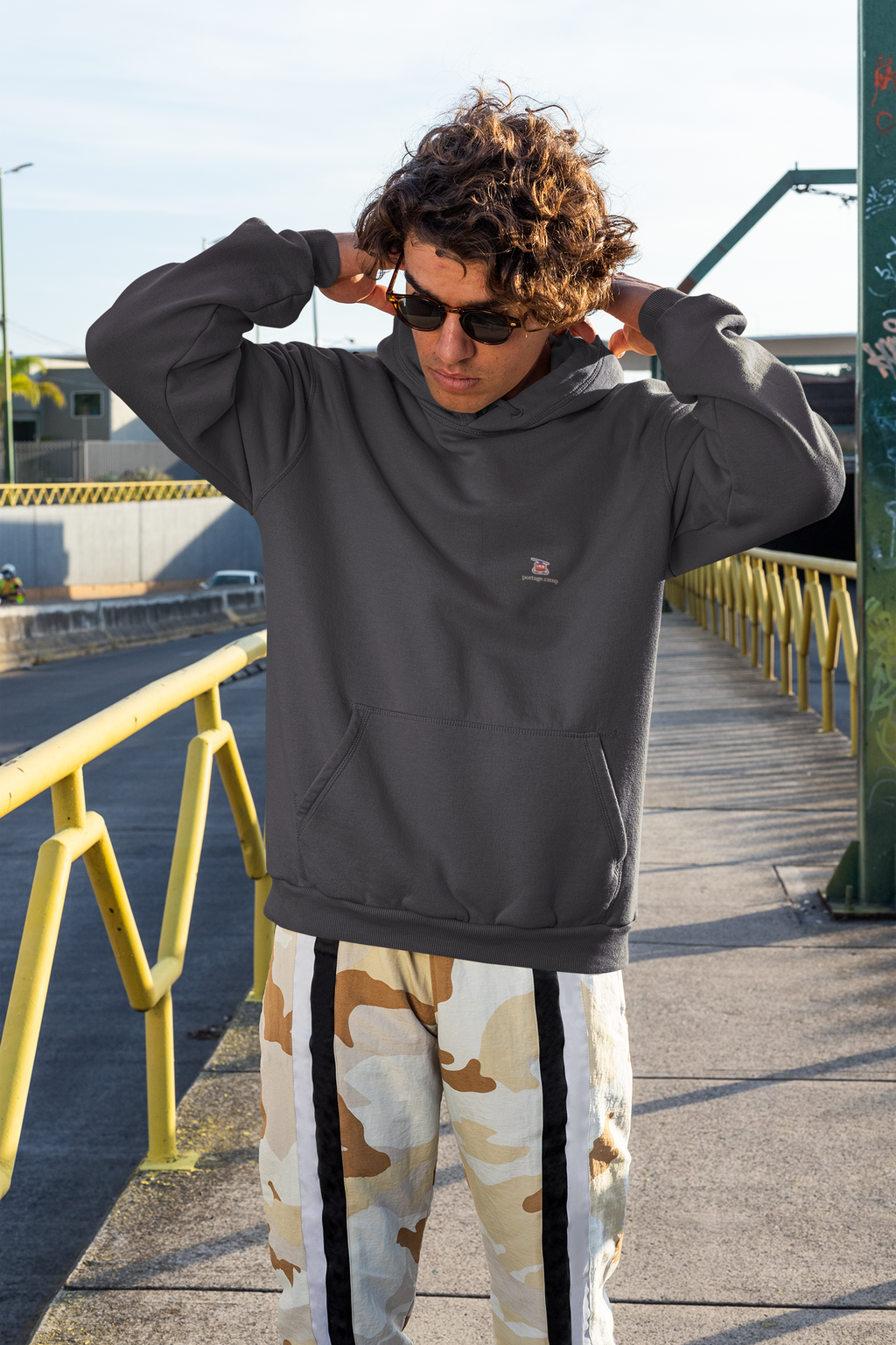 Cloud Ferry Heavyweight Hoodie in Black, worn by a man on a city street, with the Cloud Ferry logo and portage.camp on the left chest. Digital product mockup.