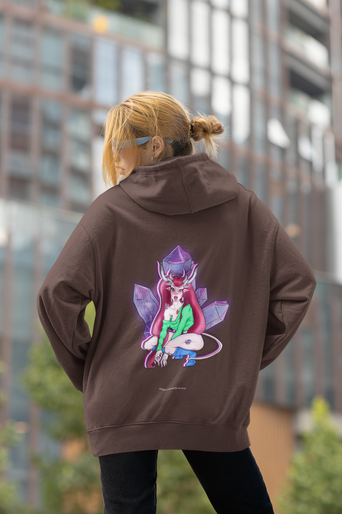 Heart Thief Heavyweight Hoodie in Brown, worn by a woman seen from behind by tall city buildings, showing the large print on the back. Digital product mockup.