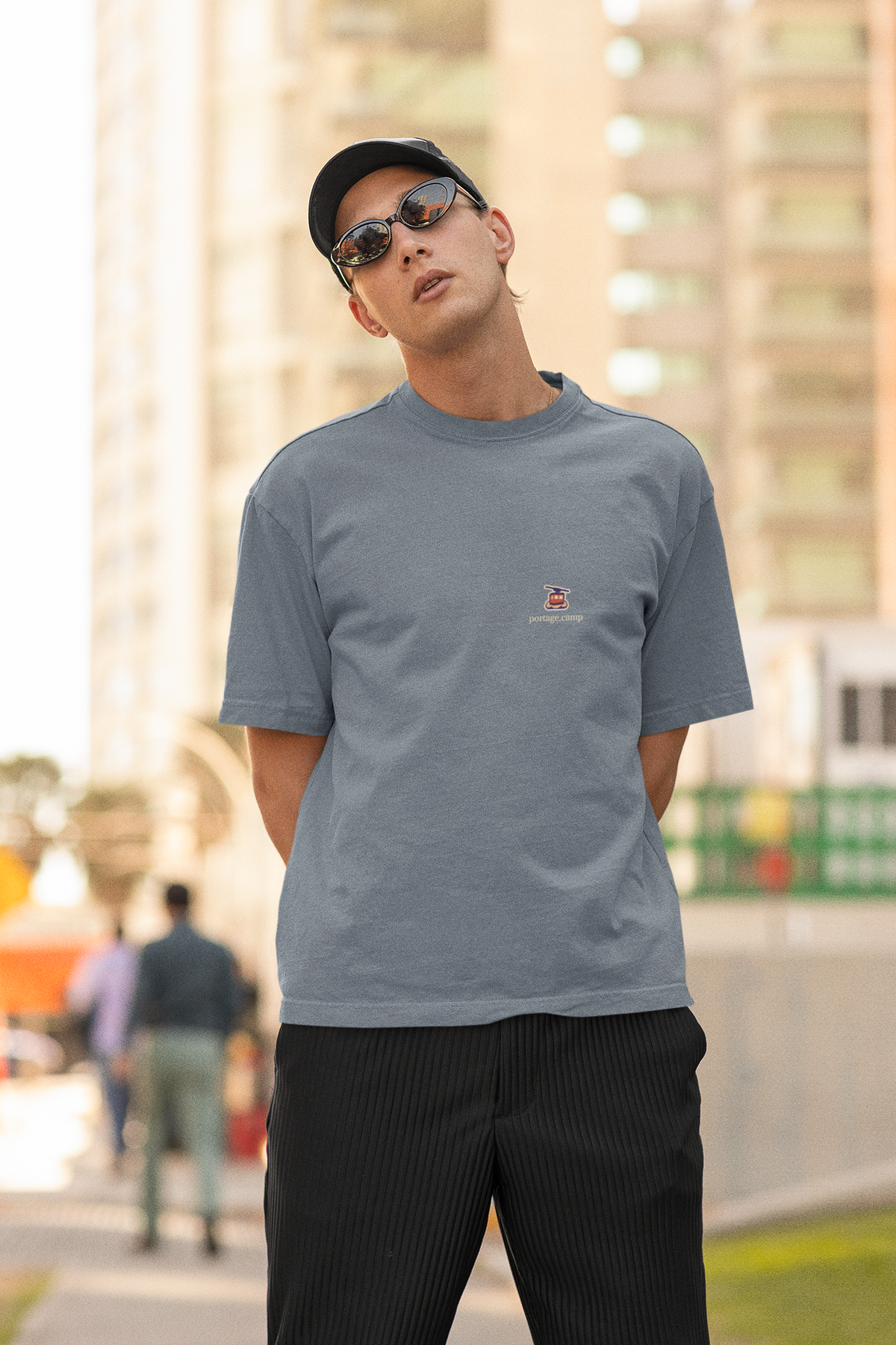 Cloud Ferry Garment-Dyed Tee in Blue Jean, worn by a man in a cap and sunglasses on a city street, with the Cloud Ferry logo and portage.camp on the chest. Digital product mockup.