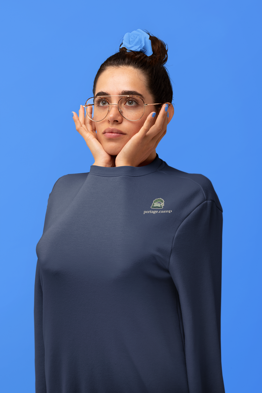 Rain Check Garment-Dyed Crewneck in True Navy, worn by a woman in a studio, arms tucked inside the sleeves, with the Rain Check logo and portage.camp on the chest. Digital product mockup.