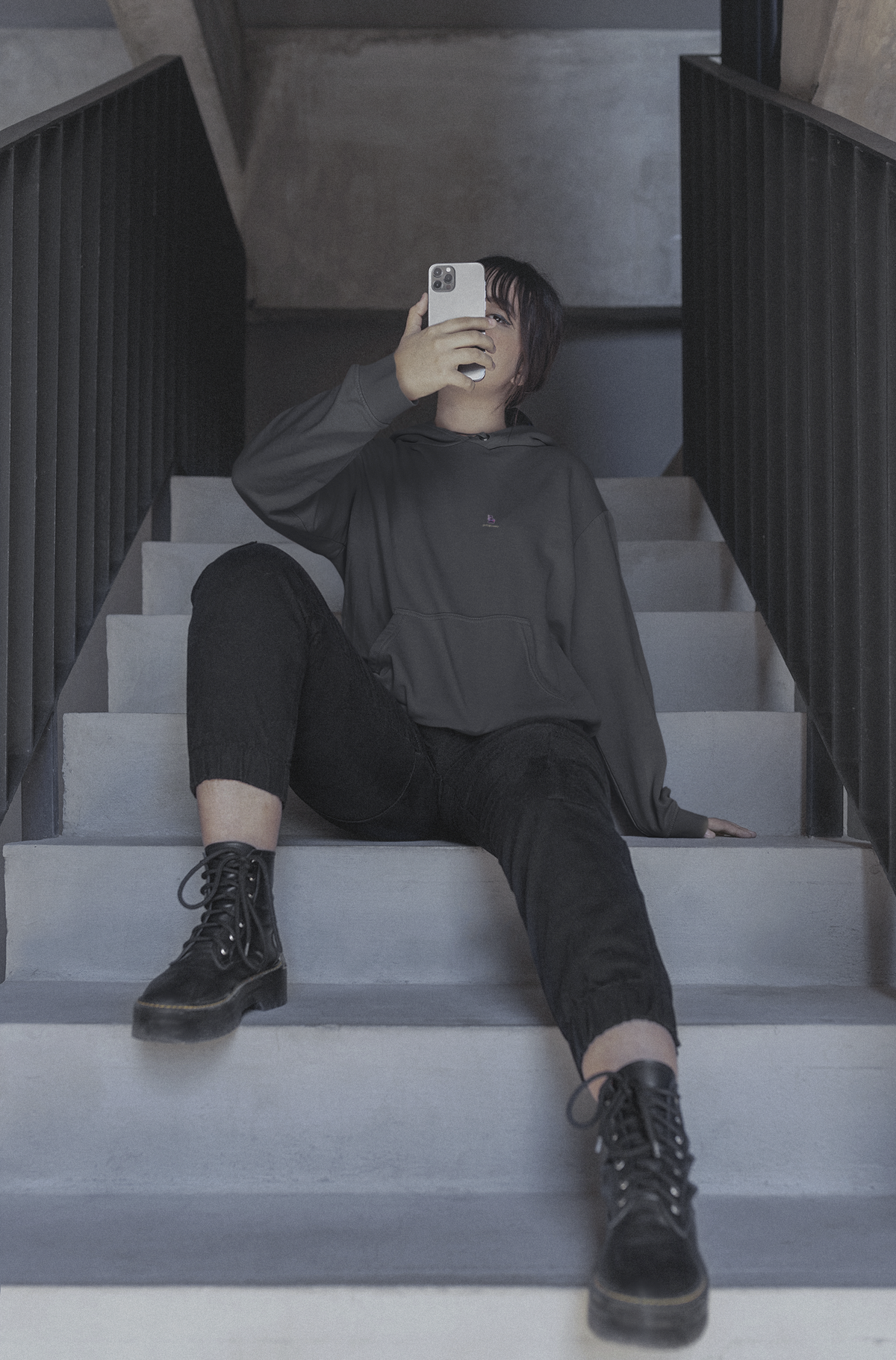 Orbit Keeper Heavyweight Hoodie in Black, worn by a woman seated on a staircase, with the Orbit Keeper logo and portage.camp on the left chest. Digital product mockup.