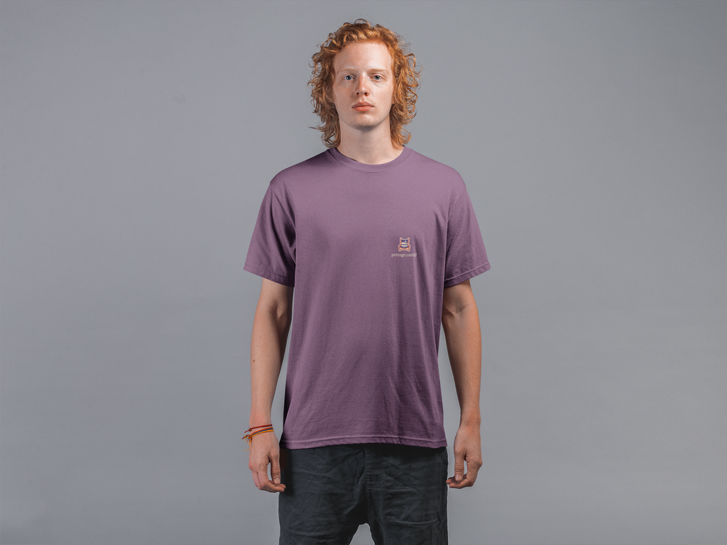 Edge of Evening Garment-Dyed Tee in Berry, worn by a man against a plain grey wall, with the Edge of Evening logo and portage.camp on the chest. Digital product mockup.