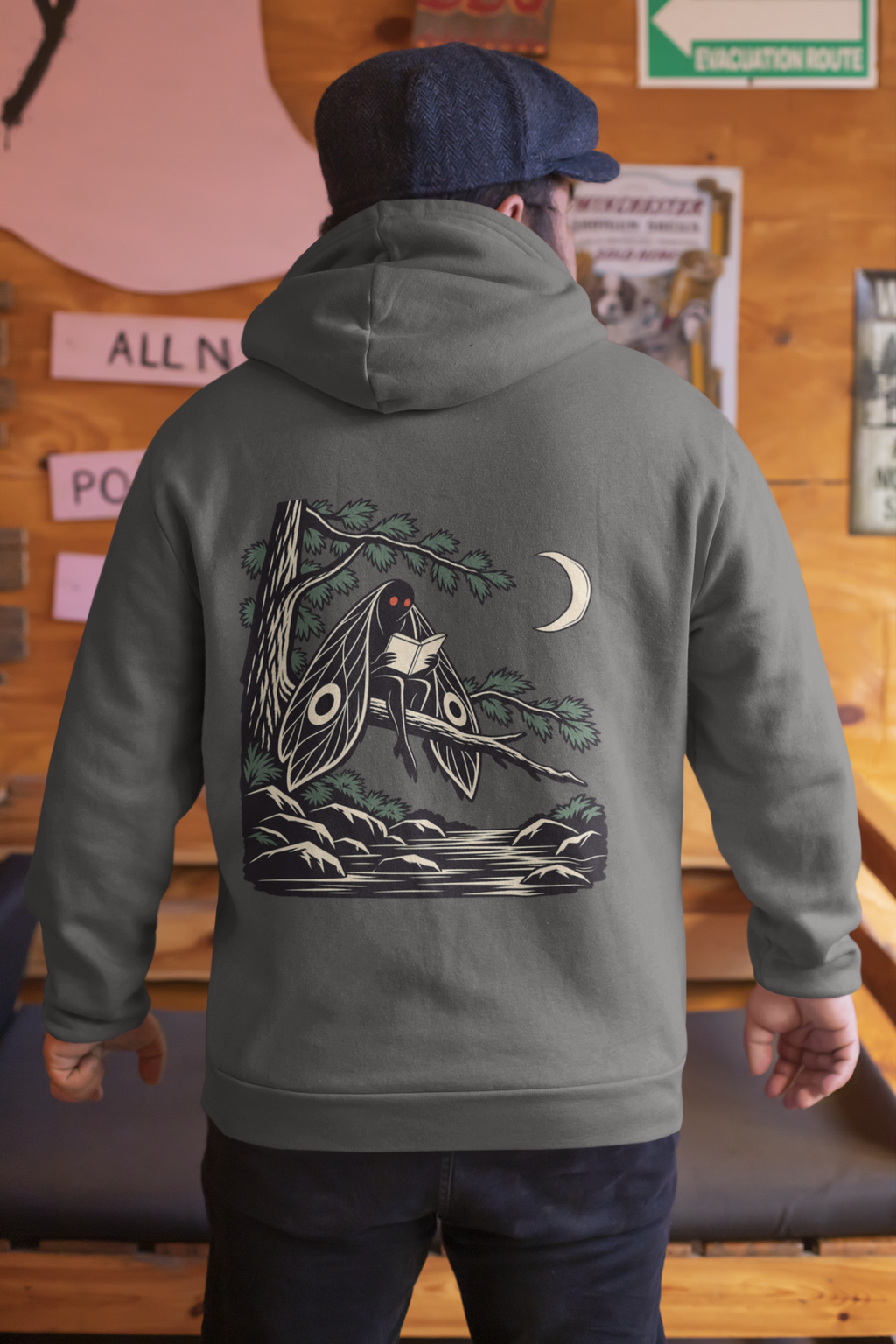Night Library Zip Hoodie in Dark Heather, worn by a man seen from behind in a wood-panelled bar, showing the large print on the back. Digital product mockup.