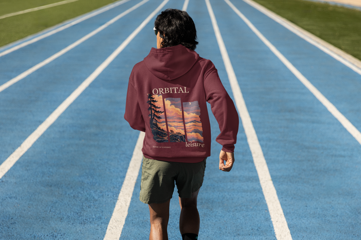 Edge of Evening Midweight Hoodie in Maroon, worn by a man seen from behind on a running track, showing the large print on the back. Digital product mockup.