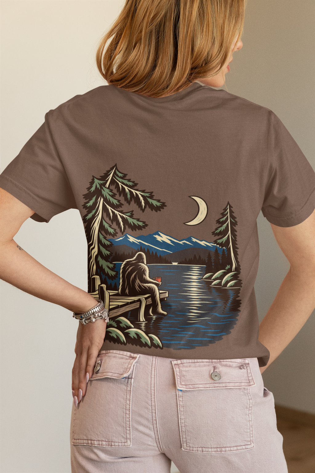 Quiet Hours Garment-Dyed Tee in Espresso, worn by a woman seen from behind in a bedroom at home, showing the large print on the back. Digital product mockup.