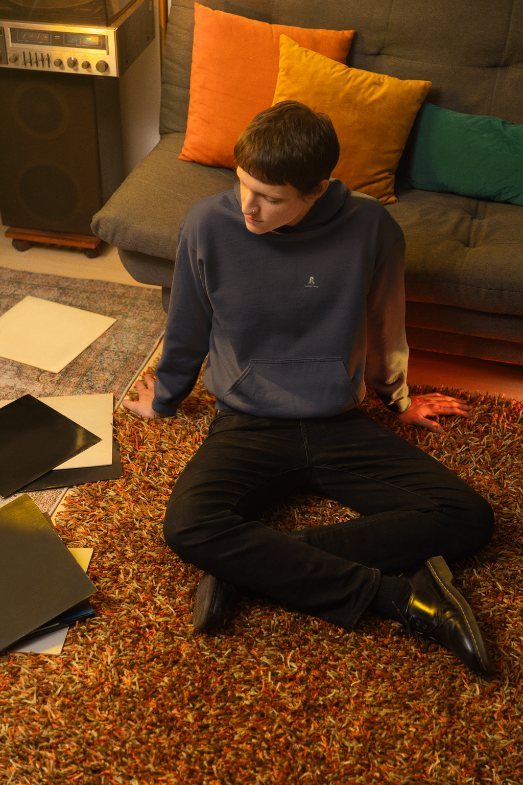 Small Hours Midweight Hoodie in Classic Navy, worn by a man seated on the floor among records, with the Small Hours logo and portage.camp on the chest. Digital product mockup.