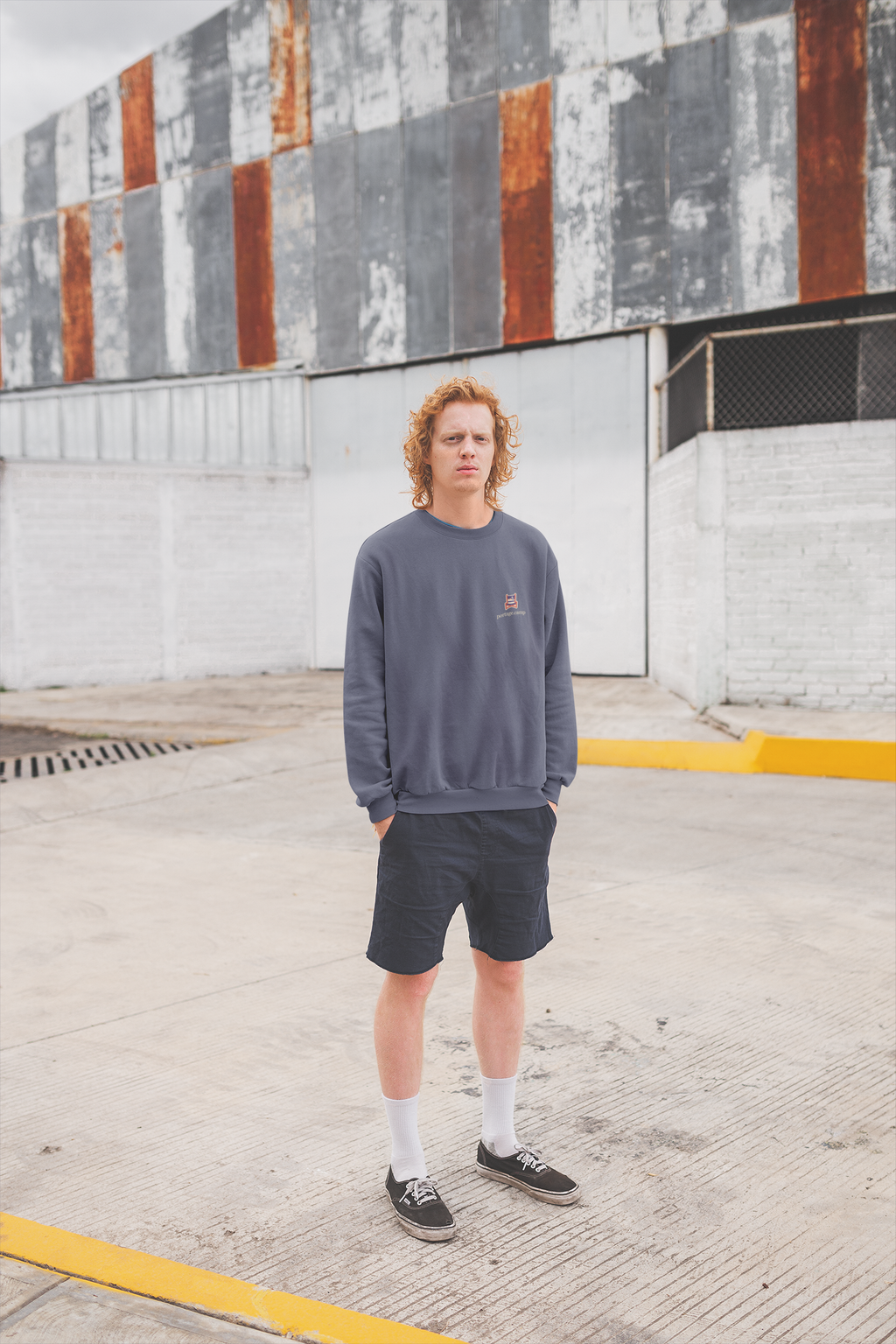 Edge of Evening Garment-Dyed Crewneck in Denim, worn by a man against a plain wall, with the Edge of Evening logo and portage.camp on the chest. Digital product mockup.