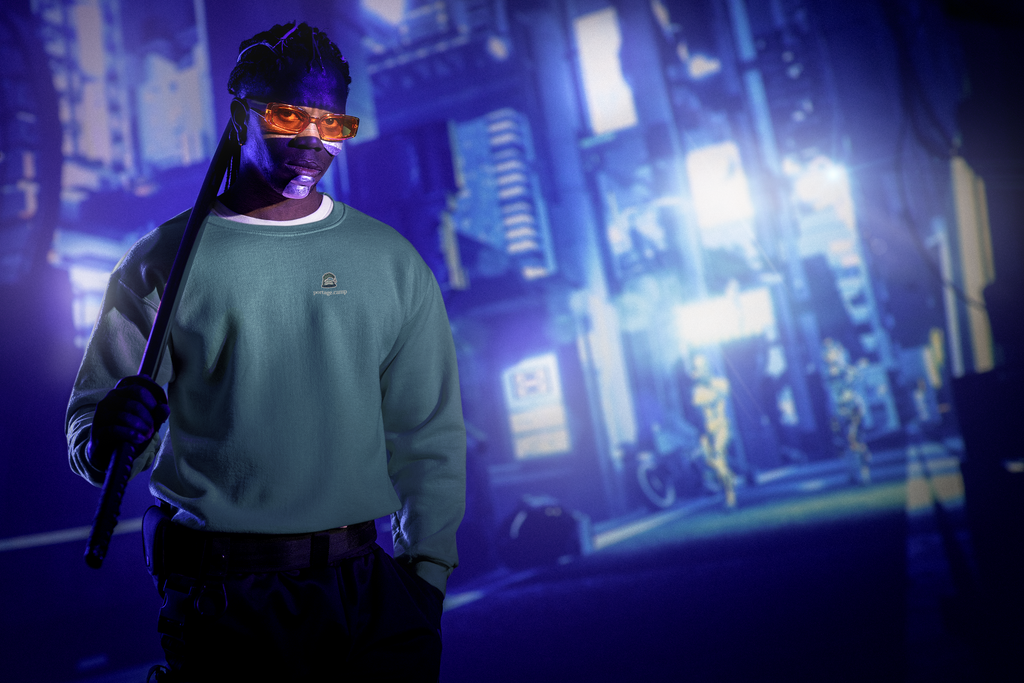 Rain Check Garment-Dyed Crewneck in Blue Spruce, worn by a man under neon city lights, with the Rain Check logo and portage.camp on the chest. Digital product mockup.