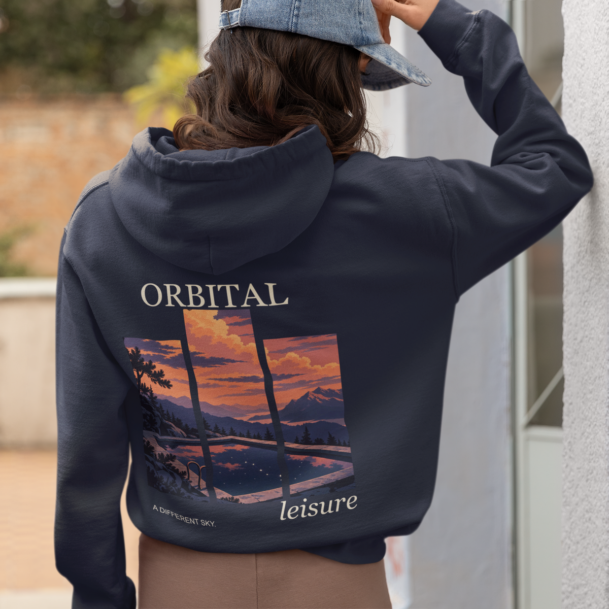 A Different Sky Zip Hoodie in Navy, worn by a woman seen from behind at home, showing the large print on the back. Digital product mockup.
