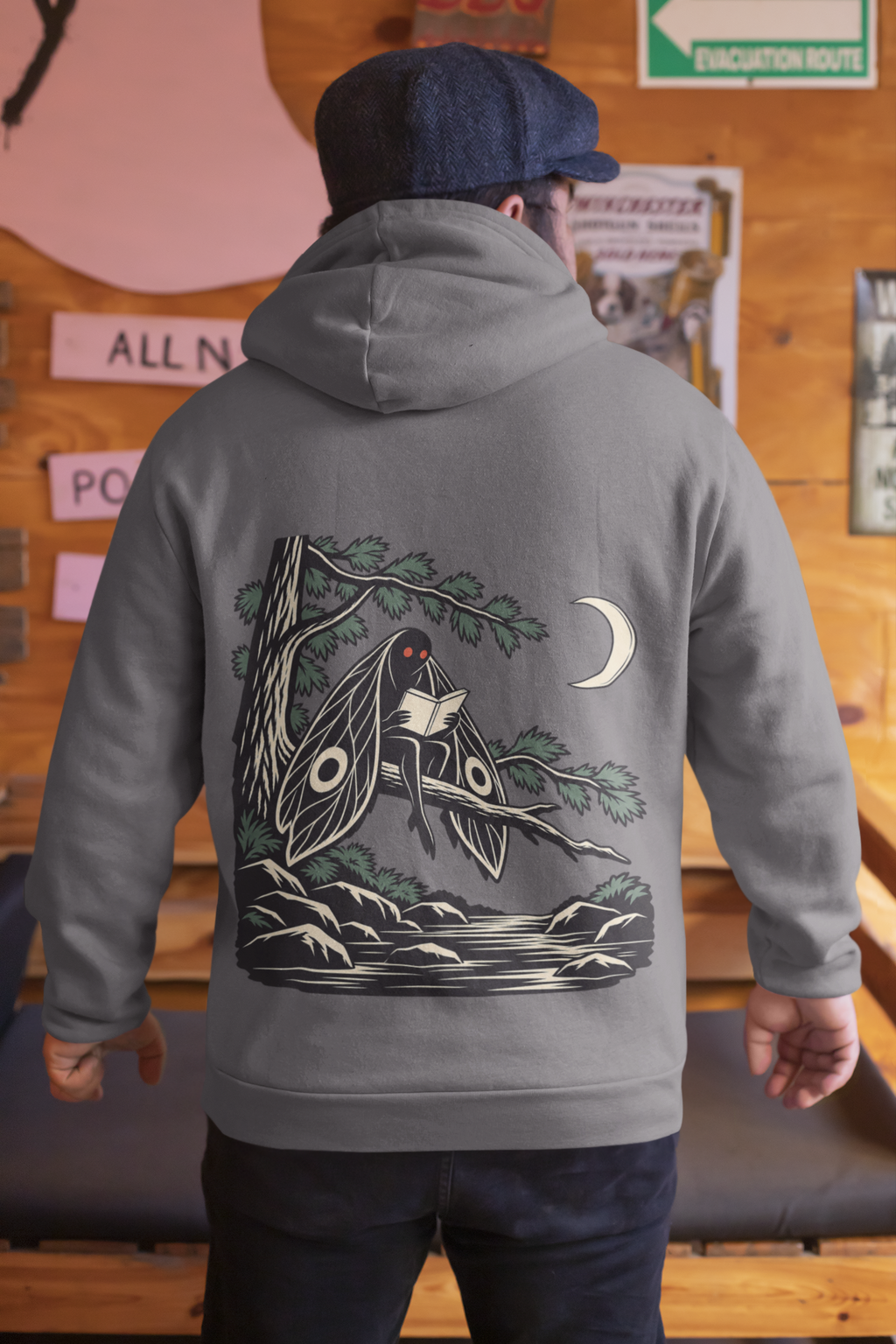 Night Library Midweight Hoodie in Charcoal, worn by a man seen from behind in a wood-panelled bar, showing the large print on the back. Digital product mockup.